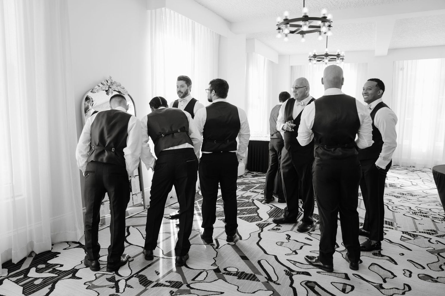 A panoramic black and white photo of wedding guests standing in a bright white reception room.