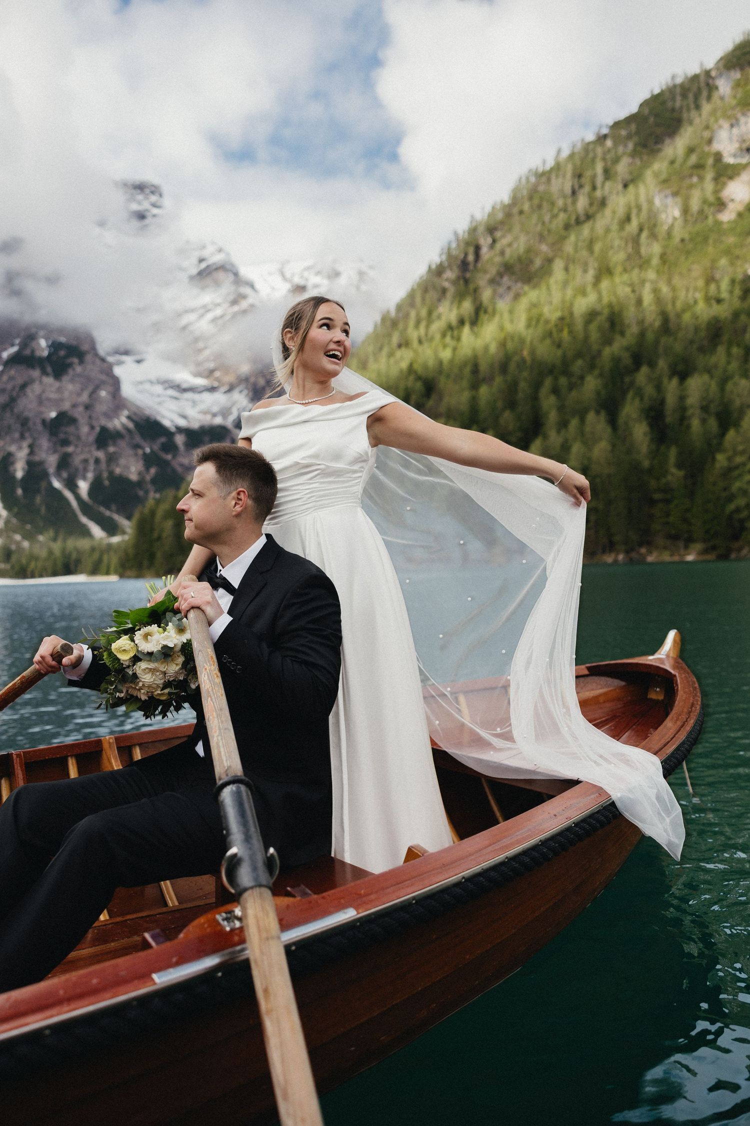 Newlyweds enjoying a romantic boat ride on alpine lake surrounded by mountain scenery.