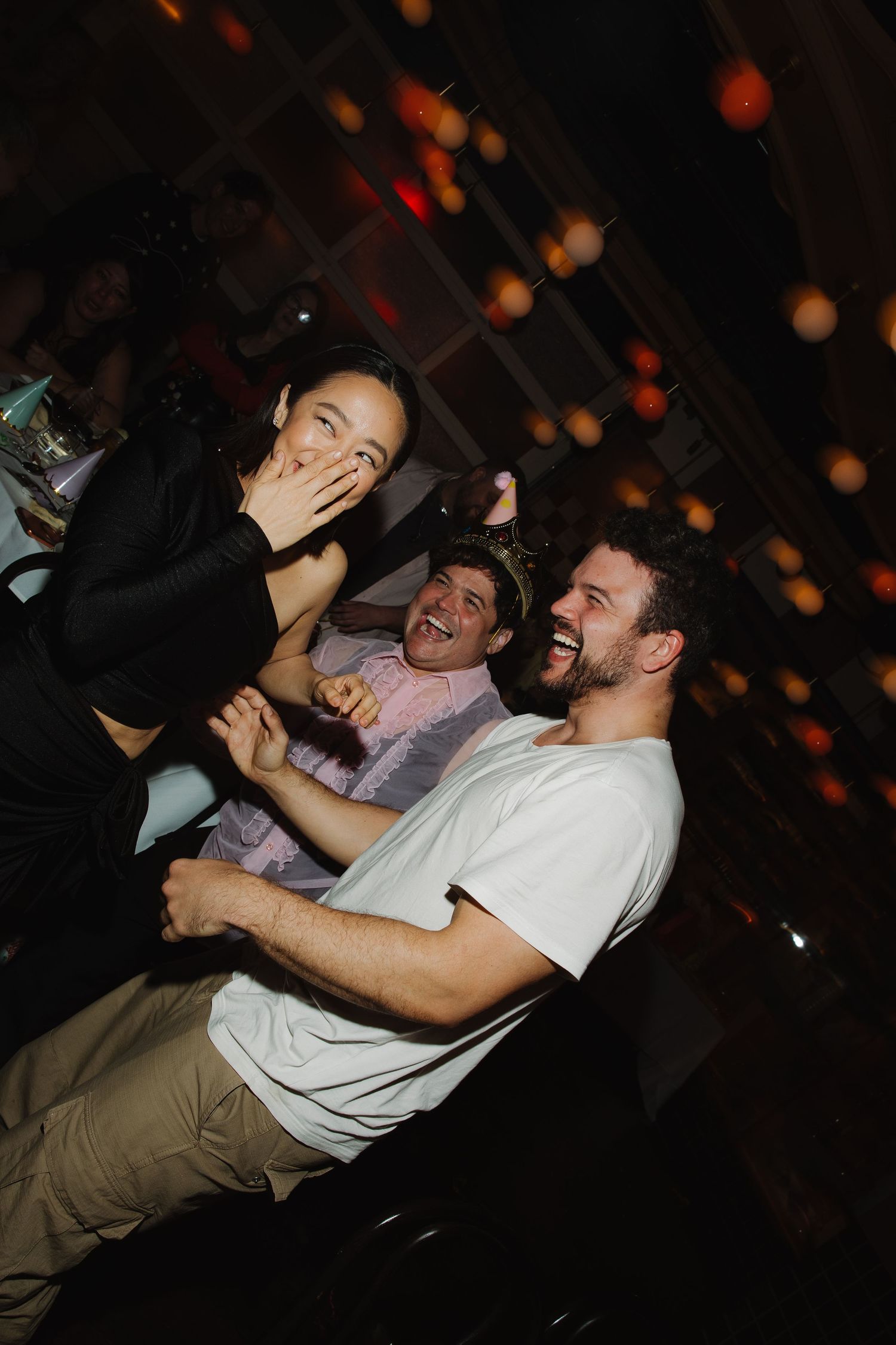 Three friends laughing and having fun together at a dimly lit party venue with bokeh lights in background.