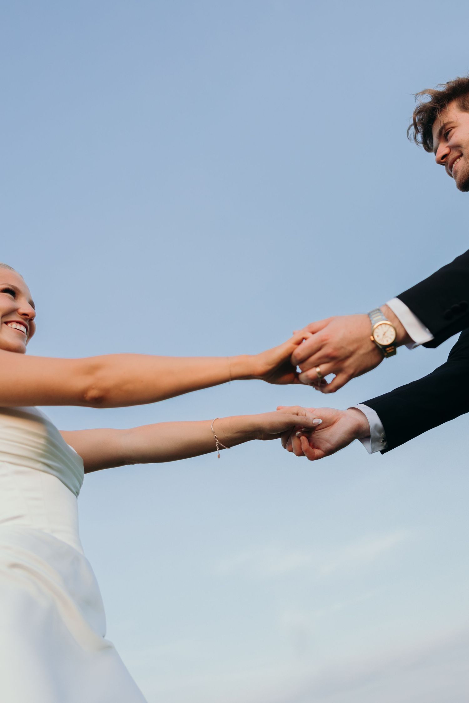 Close-up of hands reaching to hold each other against blue sky background.