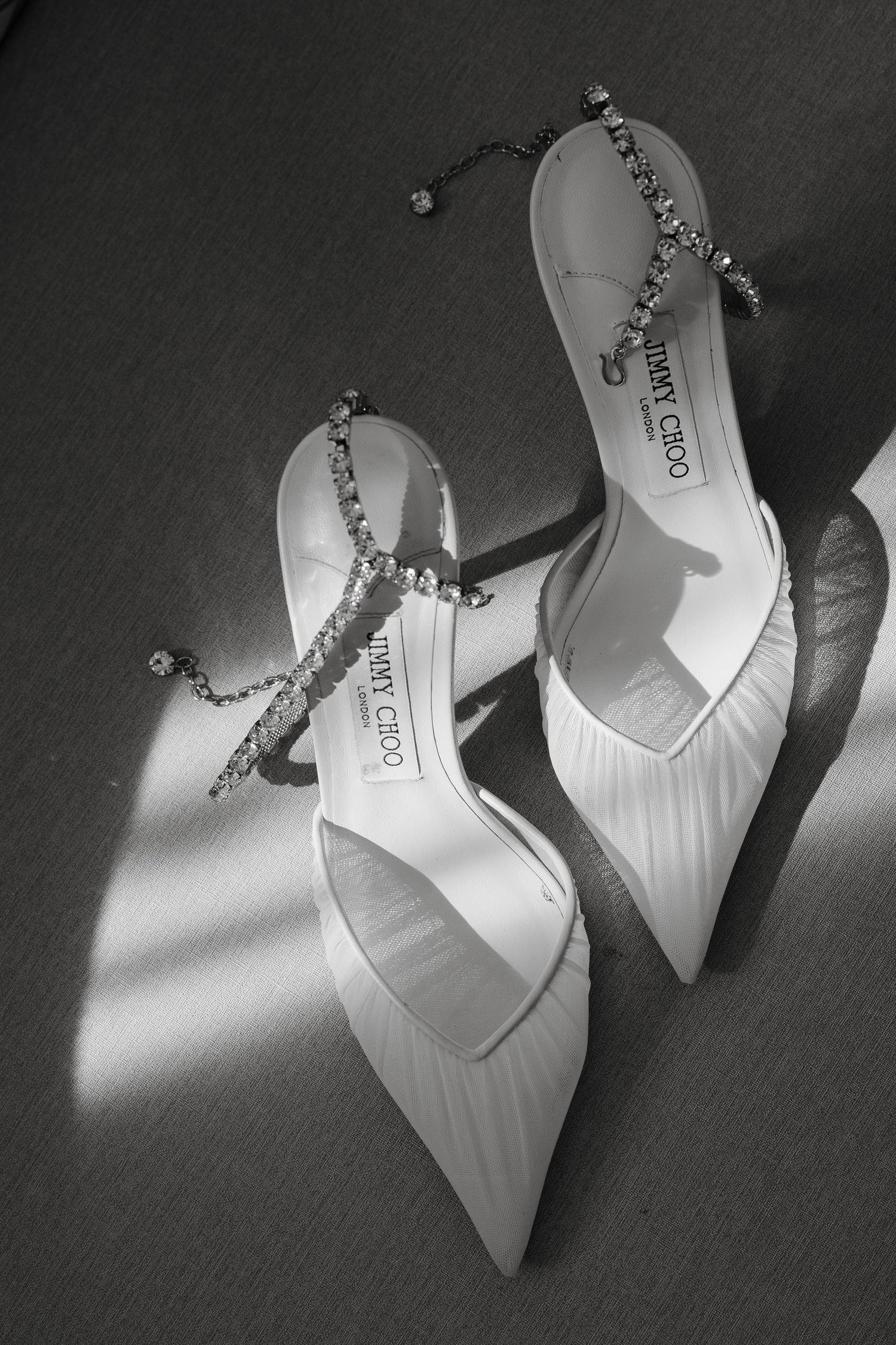 White high heel bridal shoes with delicate chain details arranged in an artistic black and white composition.