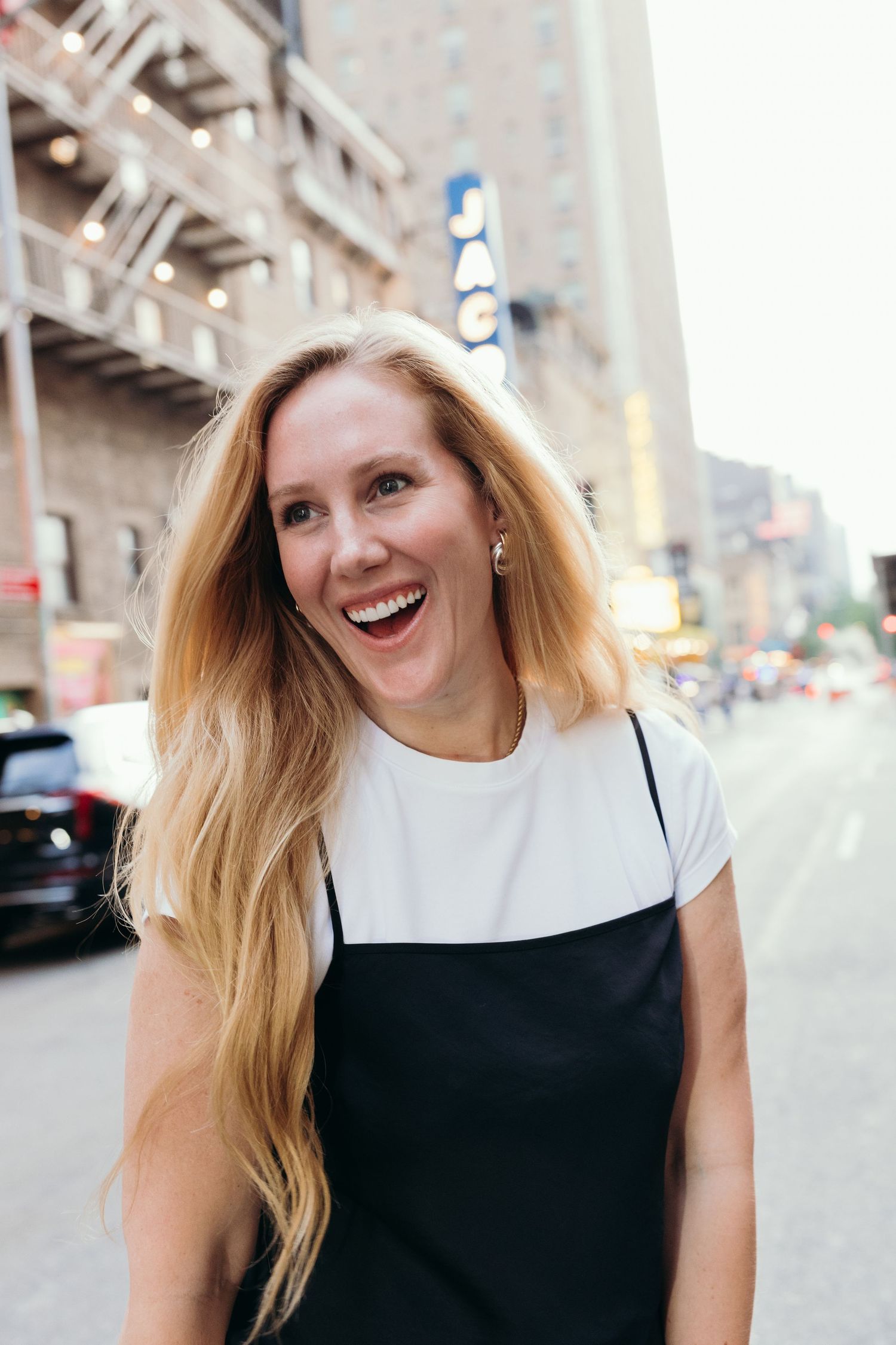 A sequence of four photos showing a joyful person with blonde hair wearing a black and white outfit on a city street.
