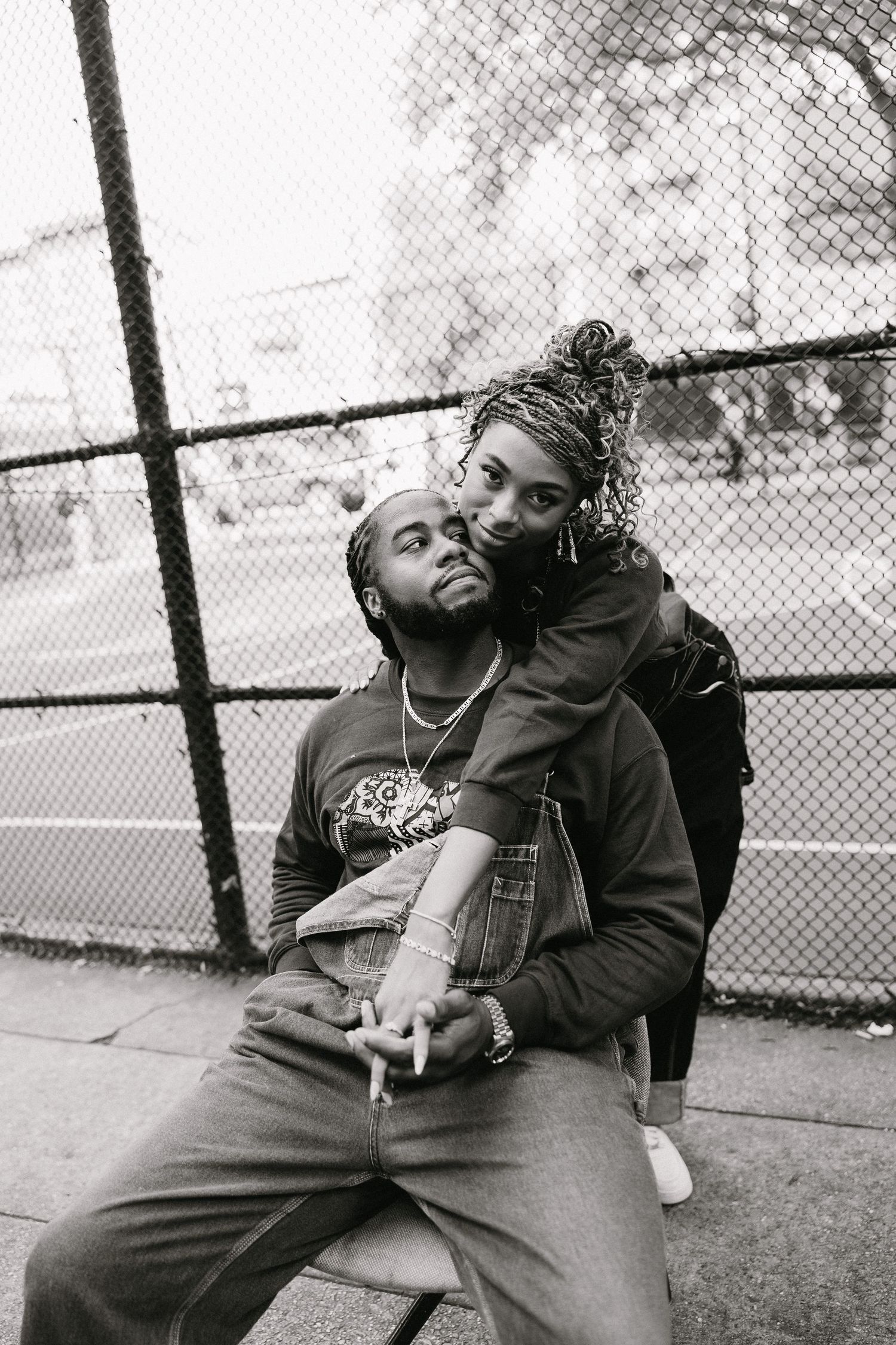 Black and white photo of two people sharing a relaxed moment by a fence.