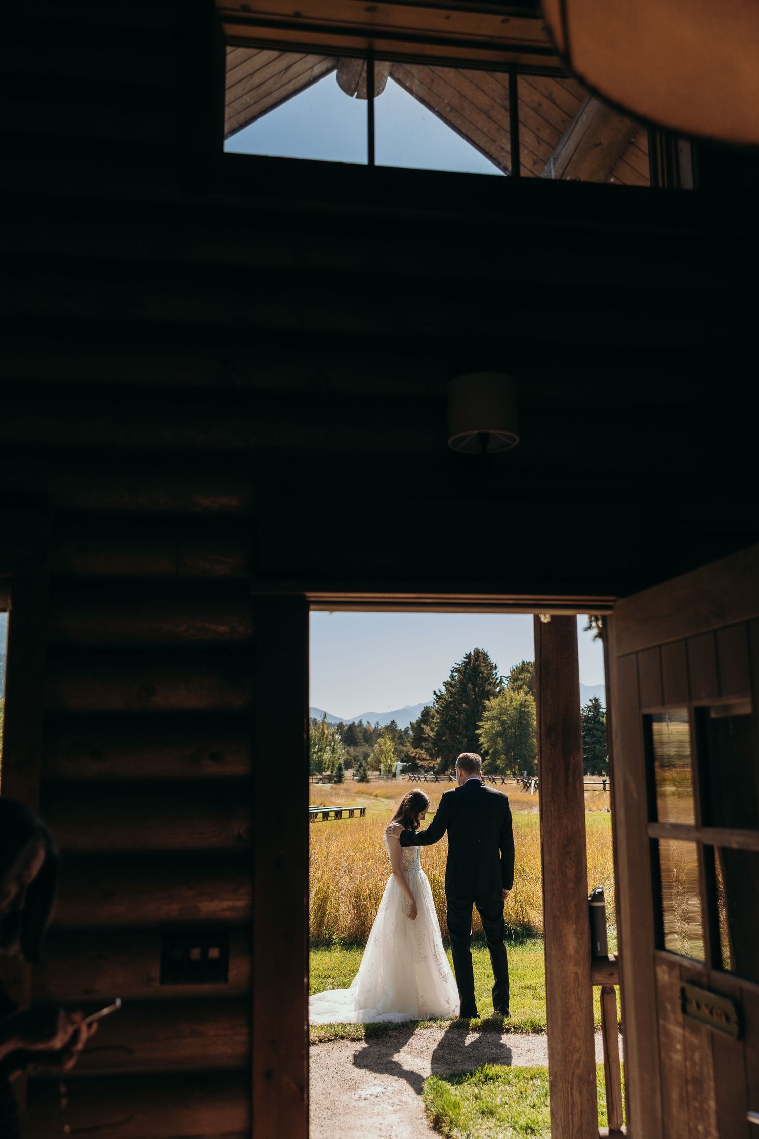 A couple shares a tender moment in silhouette against a rustic wooden backdrop during their wedding.