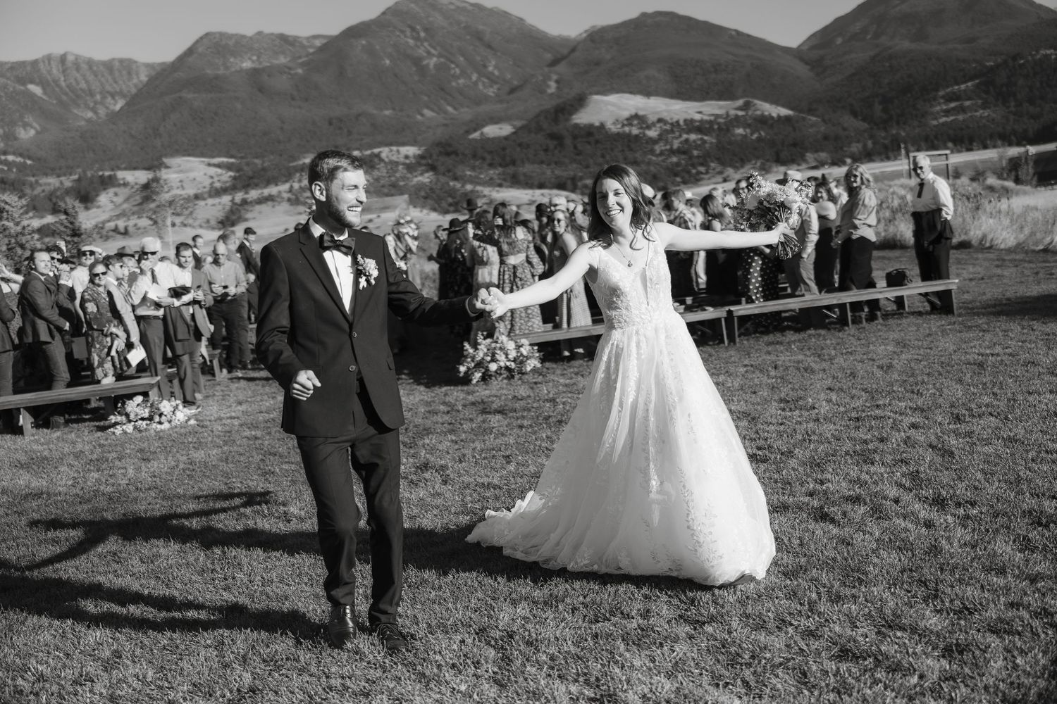 Wedding celebration in mountain meadow with guests watching from afar.
