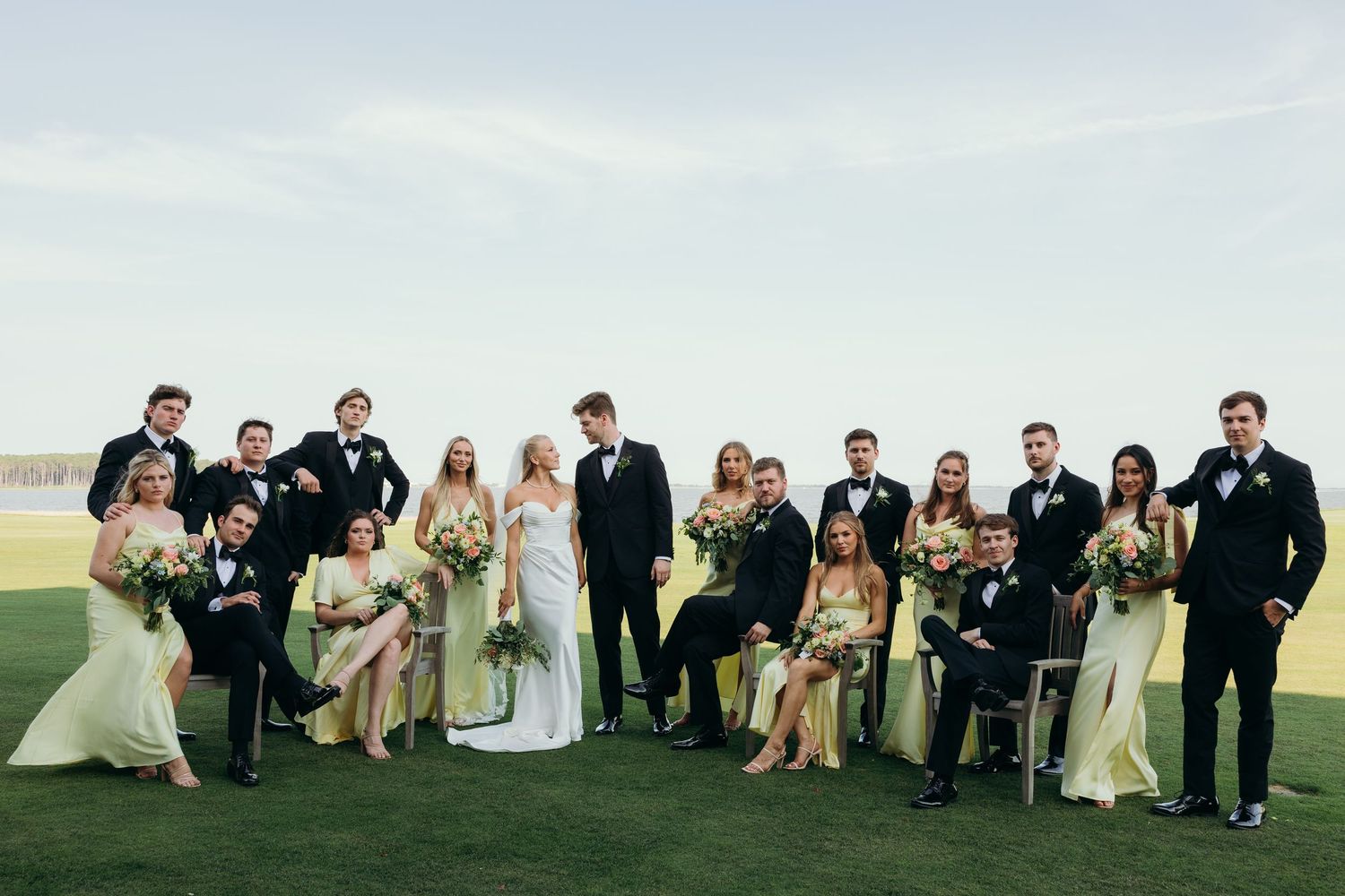 Large wedding party lounging casually on grass for a relaxed outdoor group photo.