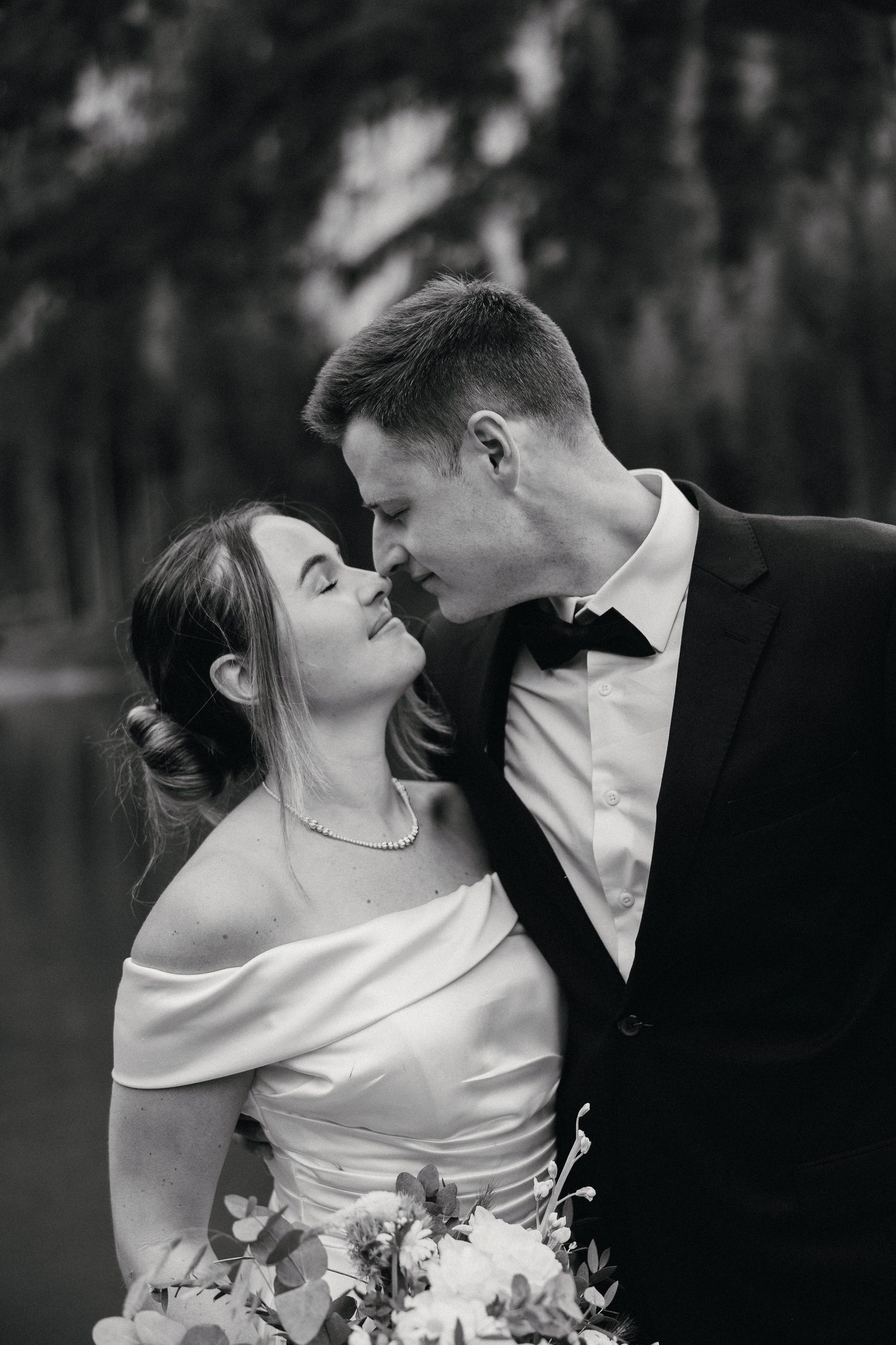 A romantic black and white wedding portrait of a couple sharing an intimate moment with the bride holding a bouquet.
