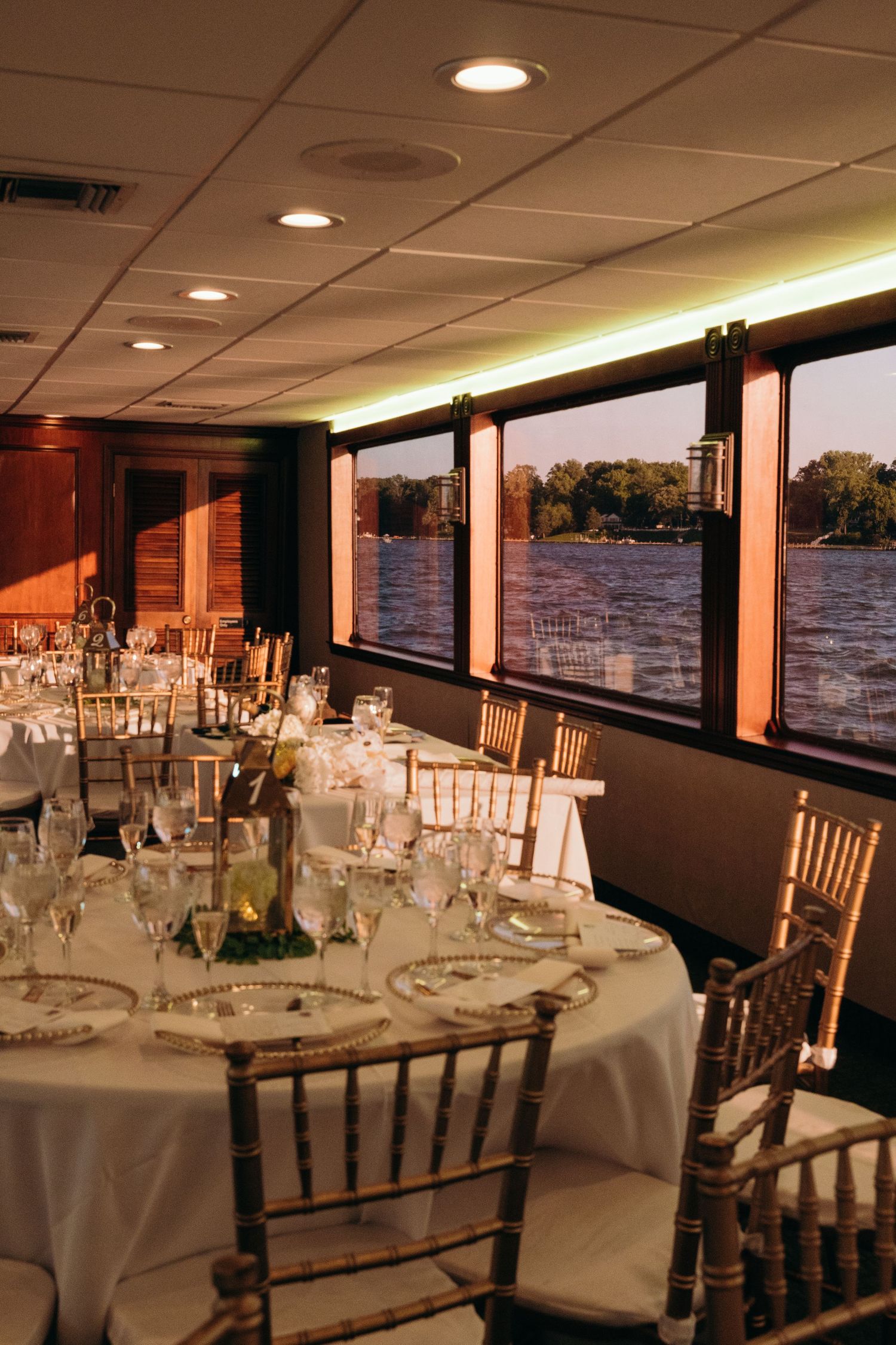 Wedding reception venue with round tables, chiavari chairs, and panoramic waterfront windows.