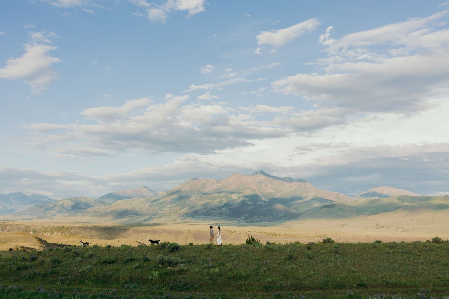 Rolling hills and mountains stretch across a scenic western landscape under a bright blue sky.