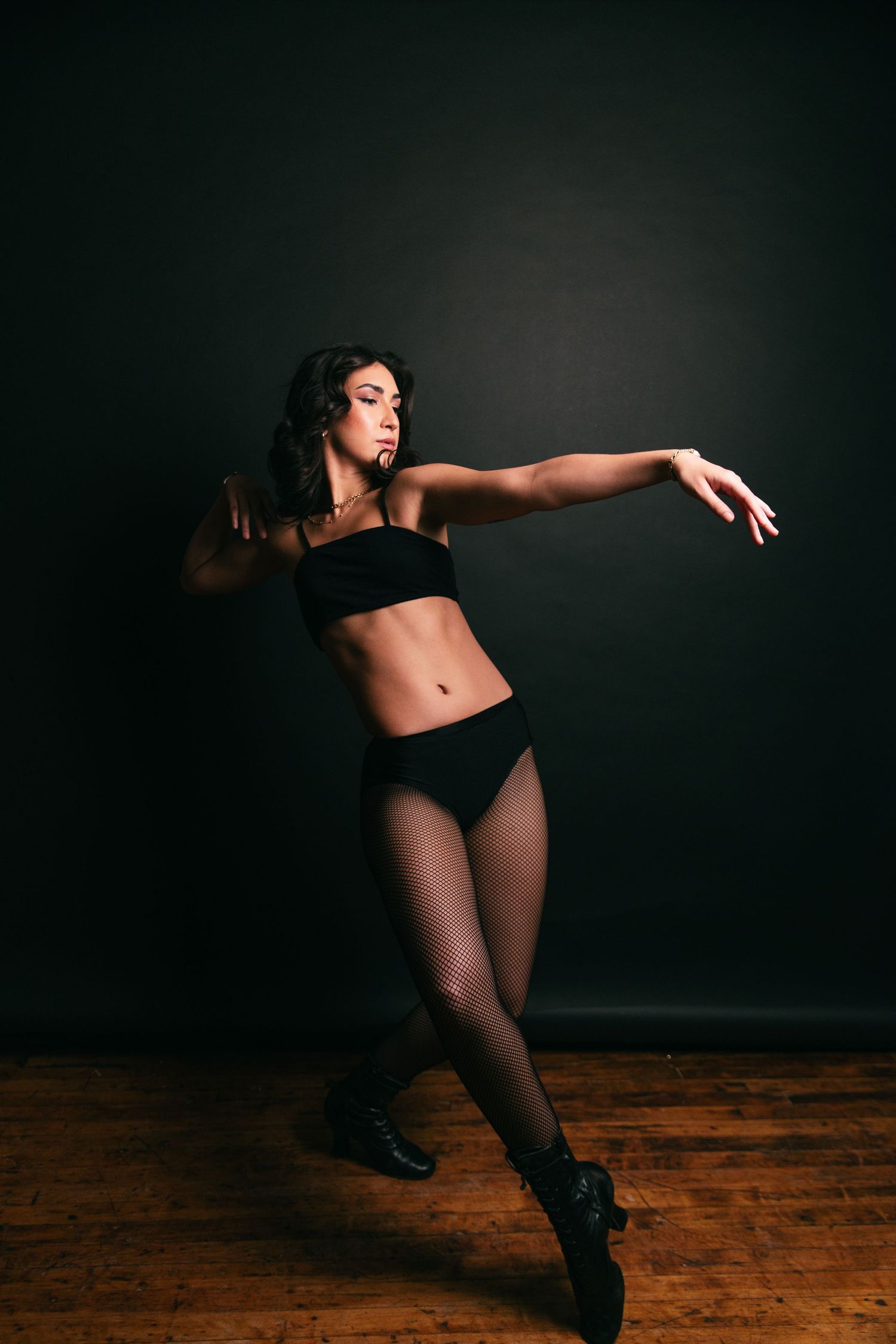 A dancer in black performs a dynamic movement sequence across a dark studio with wooden floors.