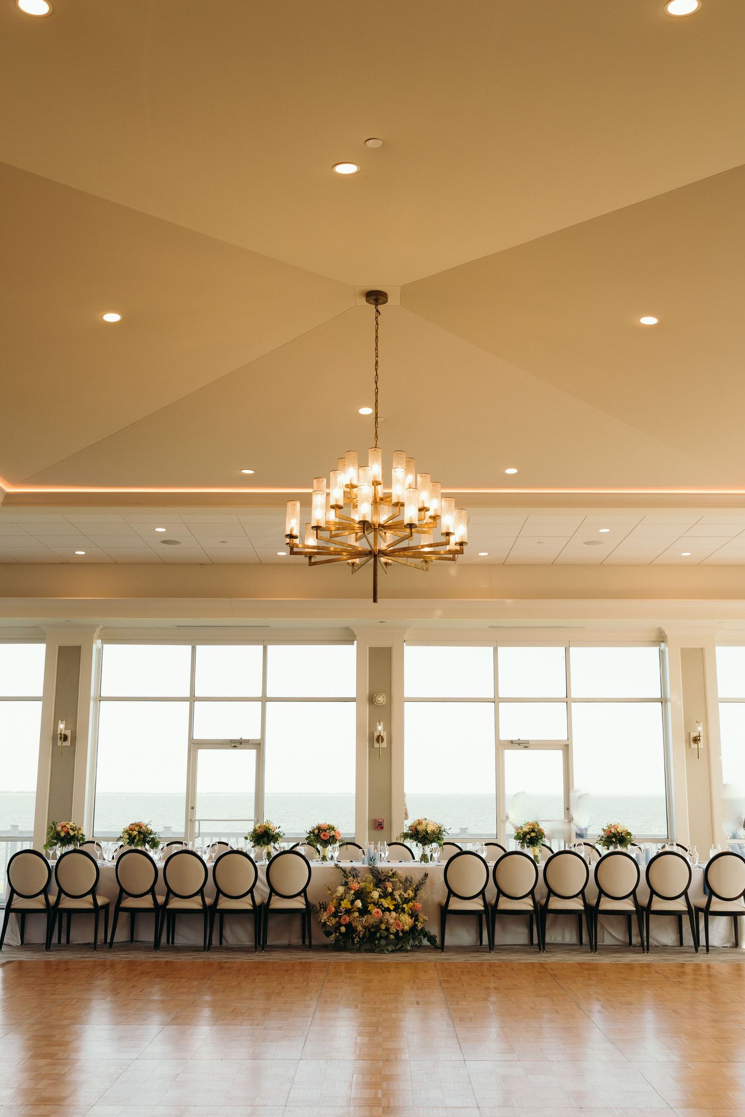 Elegant reception venue with large windows, chandeliers and rows of black and gold chairs.