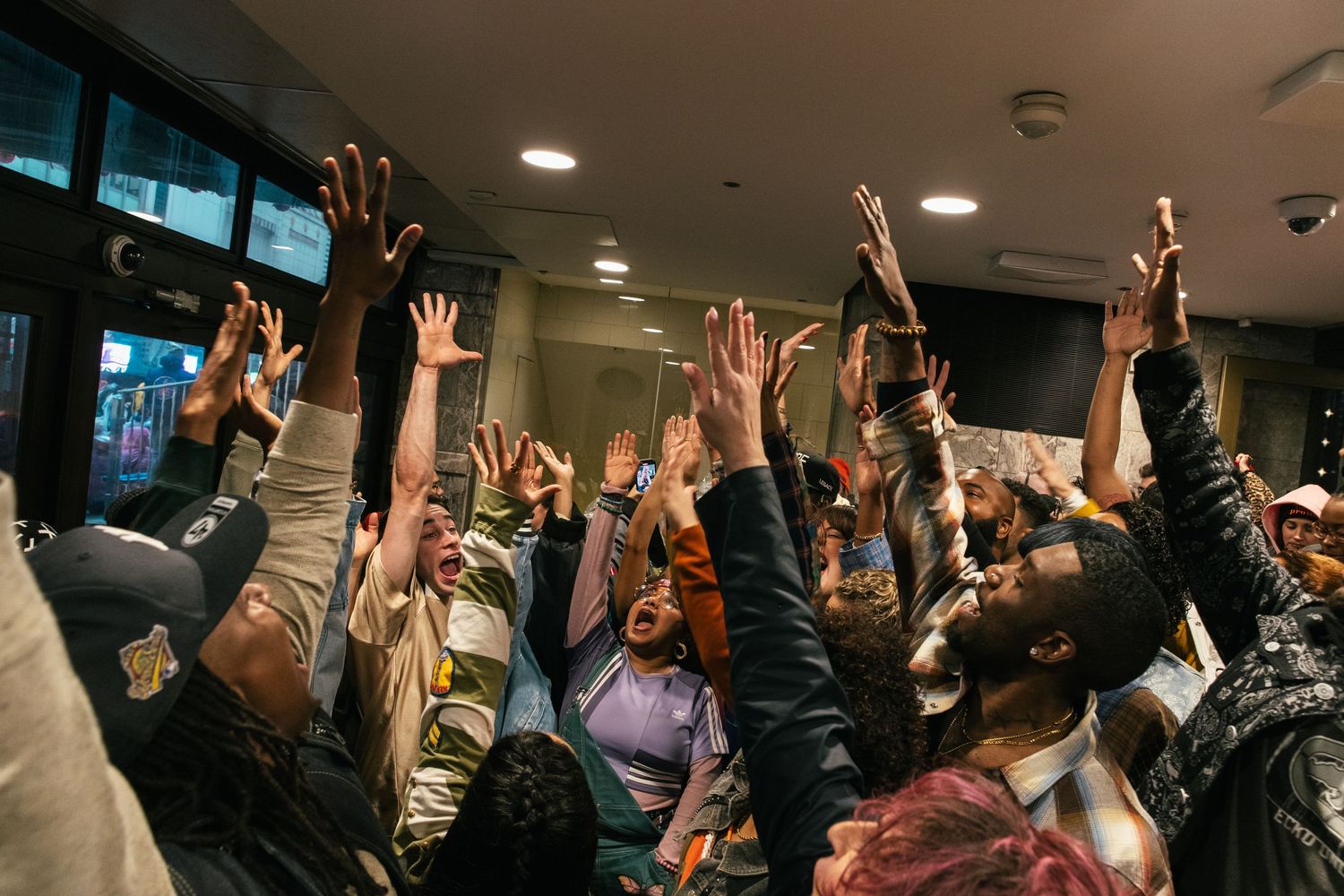 An enthusiastic crowd raises their hands in celebration at an indoor event.