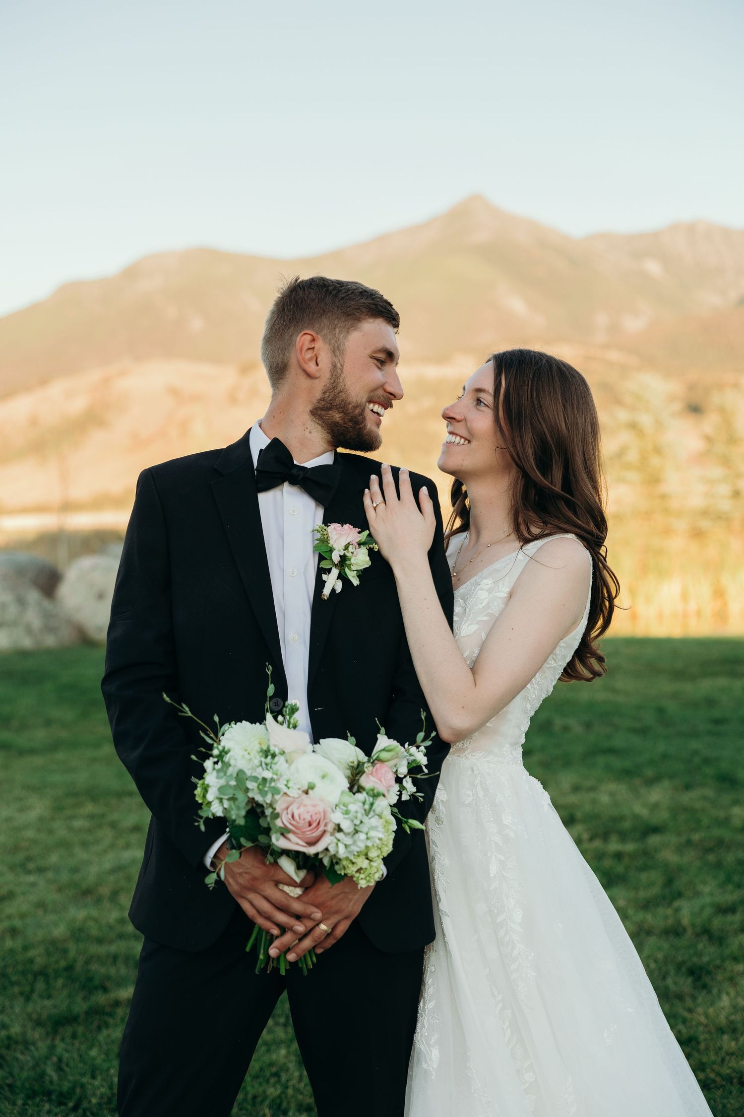 A newlywed couple shares a romantic moment with white floral bouquet against mountain backdrop.
