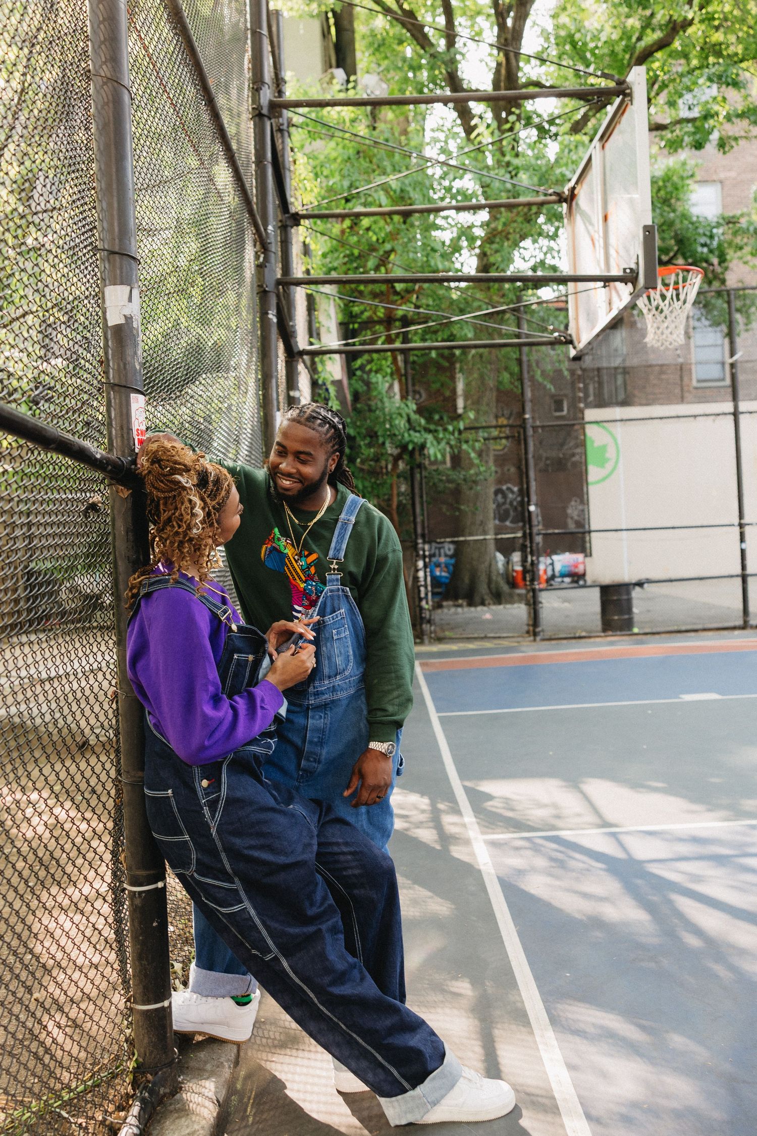 Two people share a tender moment on an outdoor basketball court surrounded by trees.