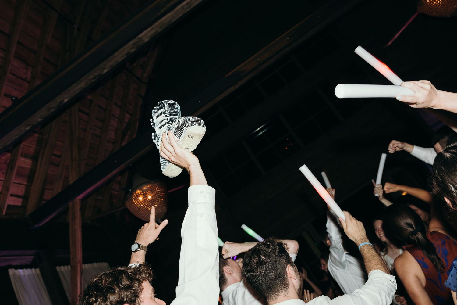 Energetic dance floor scene at a wedding reception with guests raising their hands.