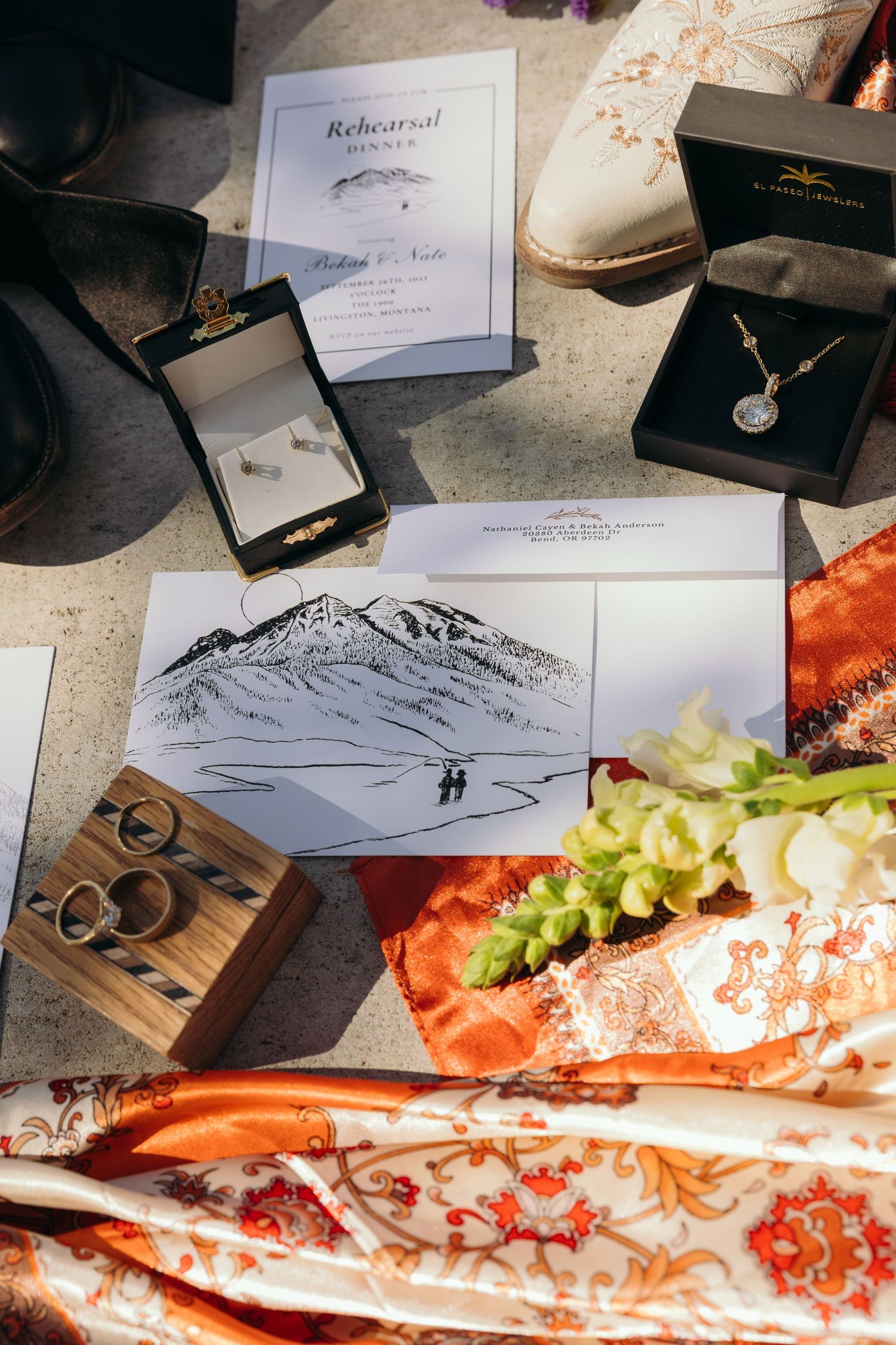 Wedding details including jewelry boxes, invitation with mountain sketch, and decorative accessories.