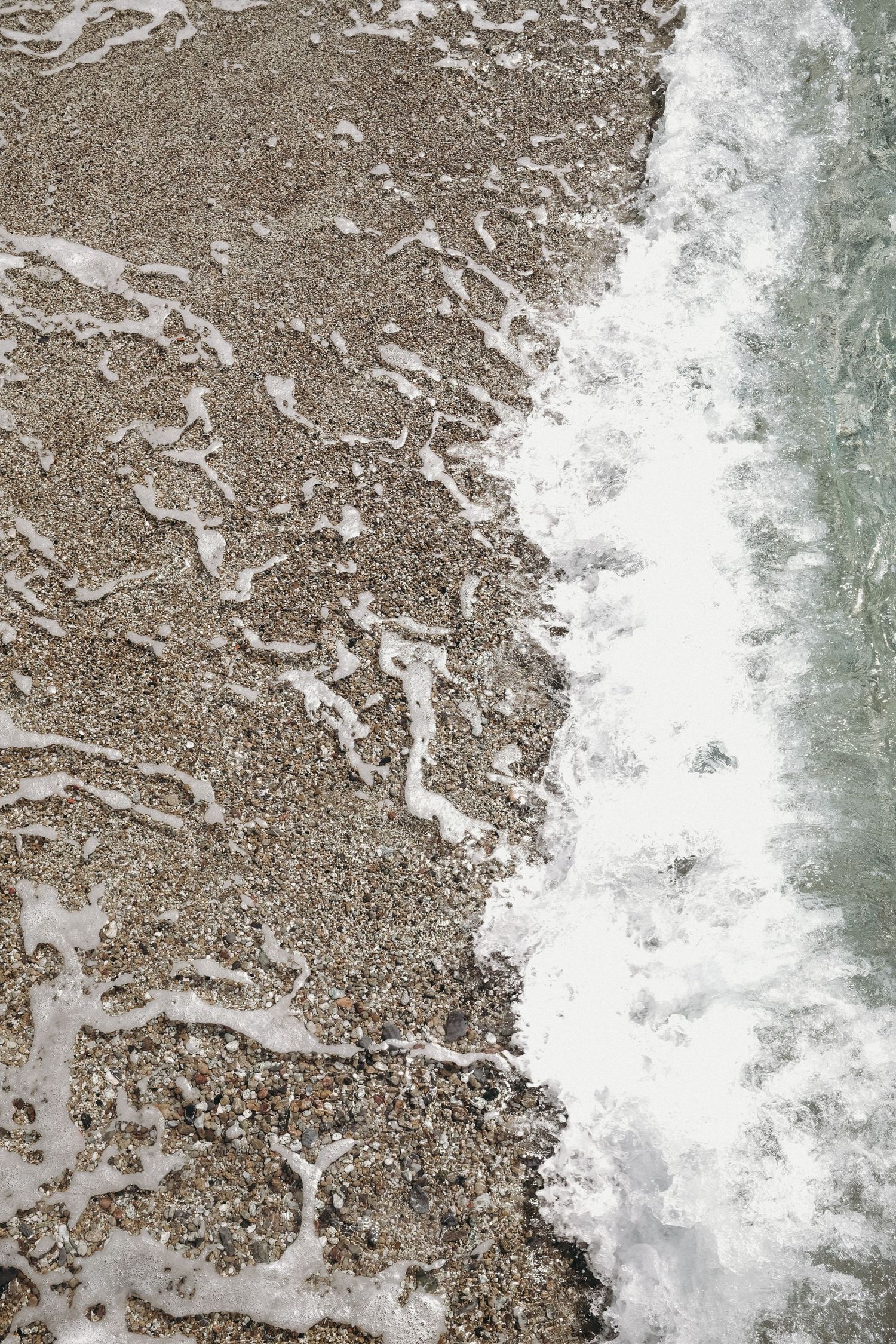 Close-up view of ocean waves crashing onto a sandy beach creating white foam patterns.