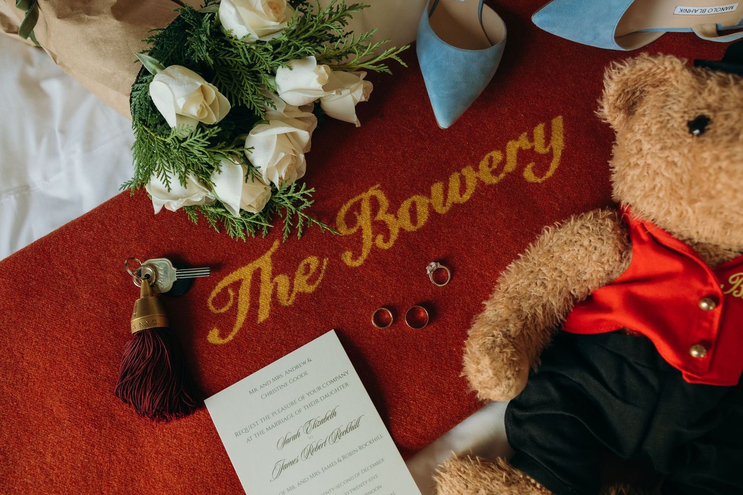 Elegant wedding invitation details displayed with white roses, greenery, and vintage decor on a red velvet background.