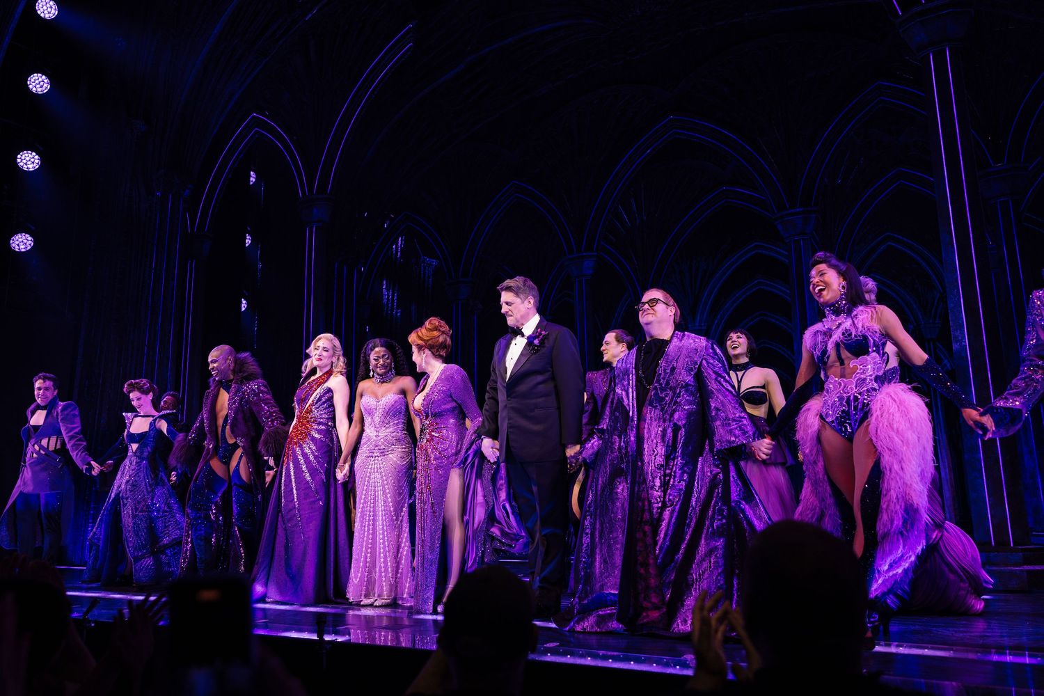 Dark stage with performers creating silhouettes against purple theatrical lighting.