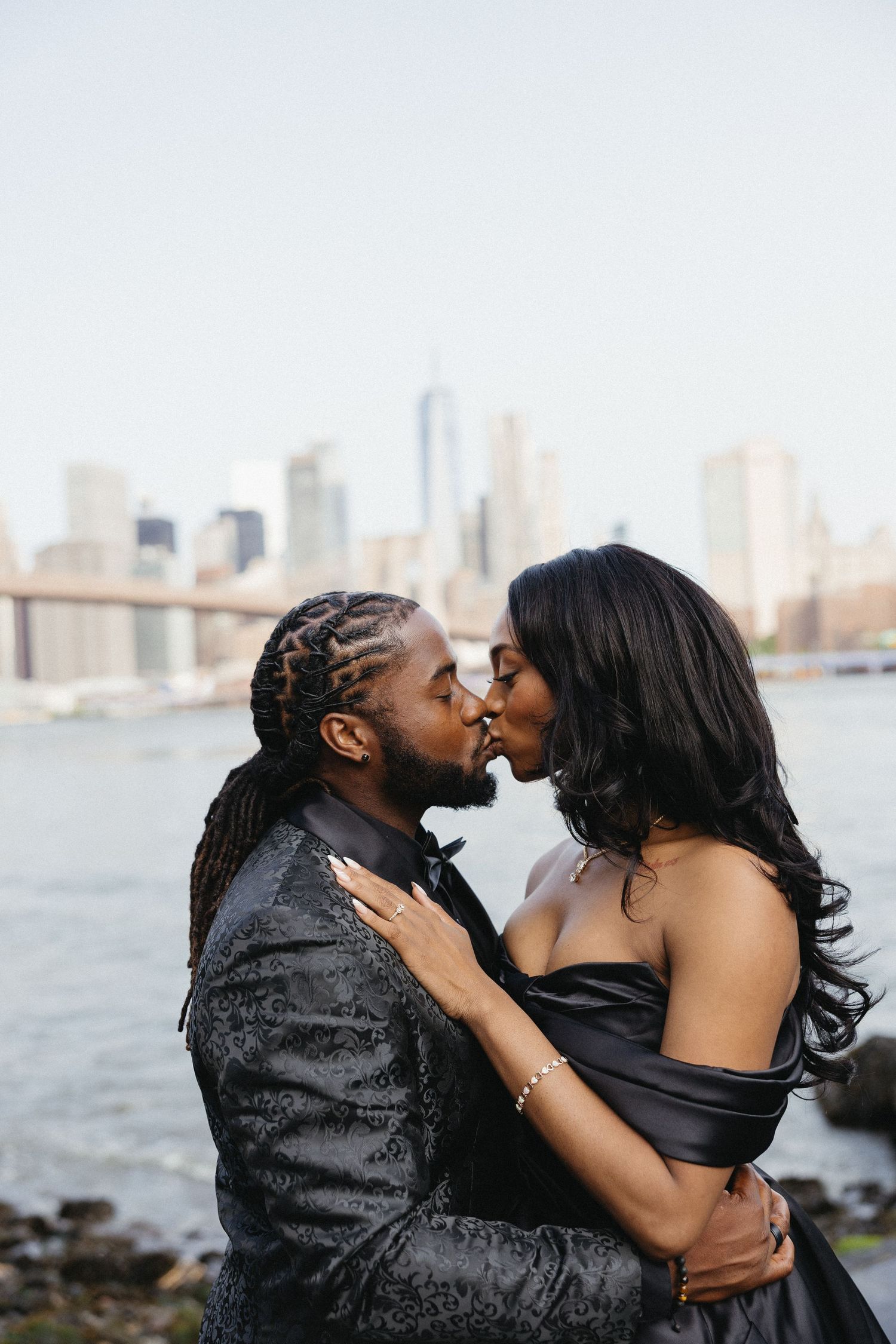 Romantic couple embraces and kisses against a waterfront cityscape backdrop.