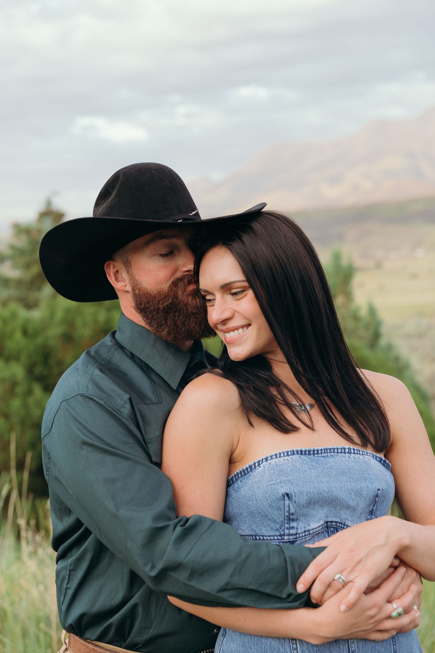 A couple shares an intimate embrace in a denim outfit against a mountain landscape.
