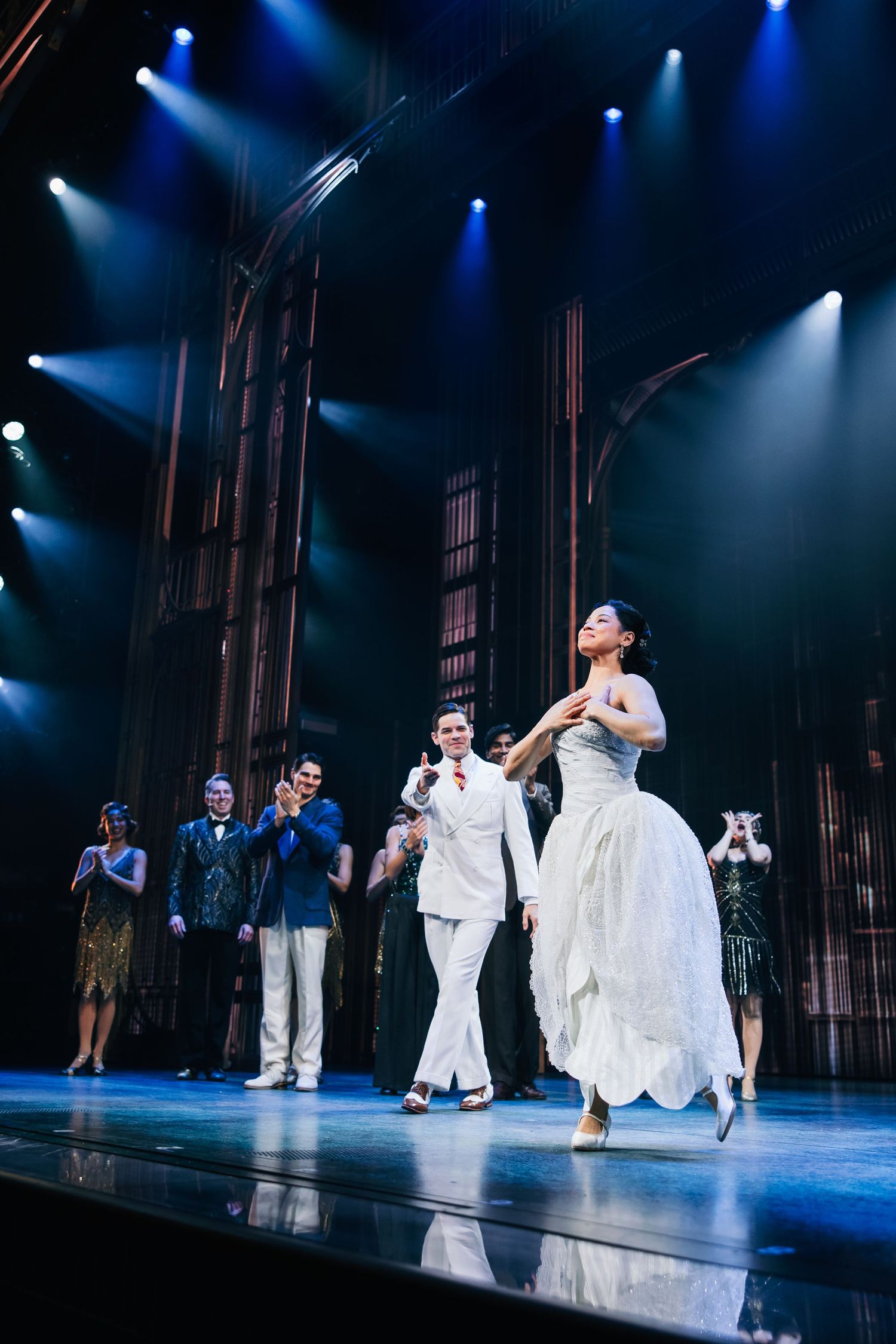 Broadway performers take a bow on stage during a theatrical production finale with dramatic blue stage lighting.