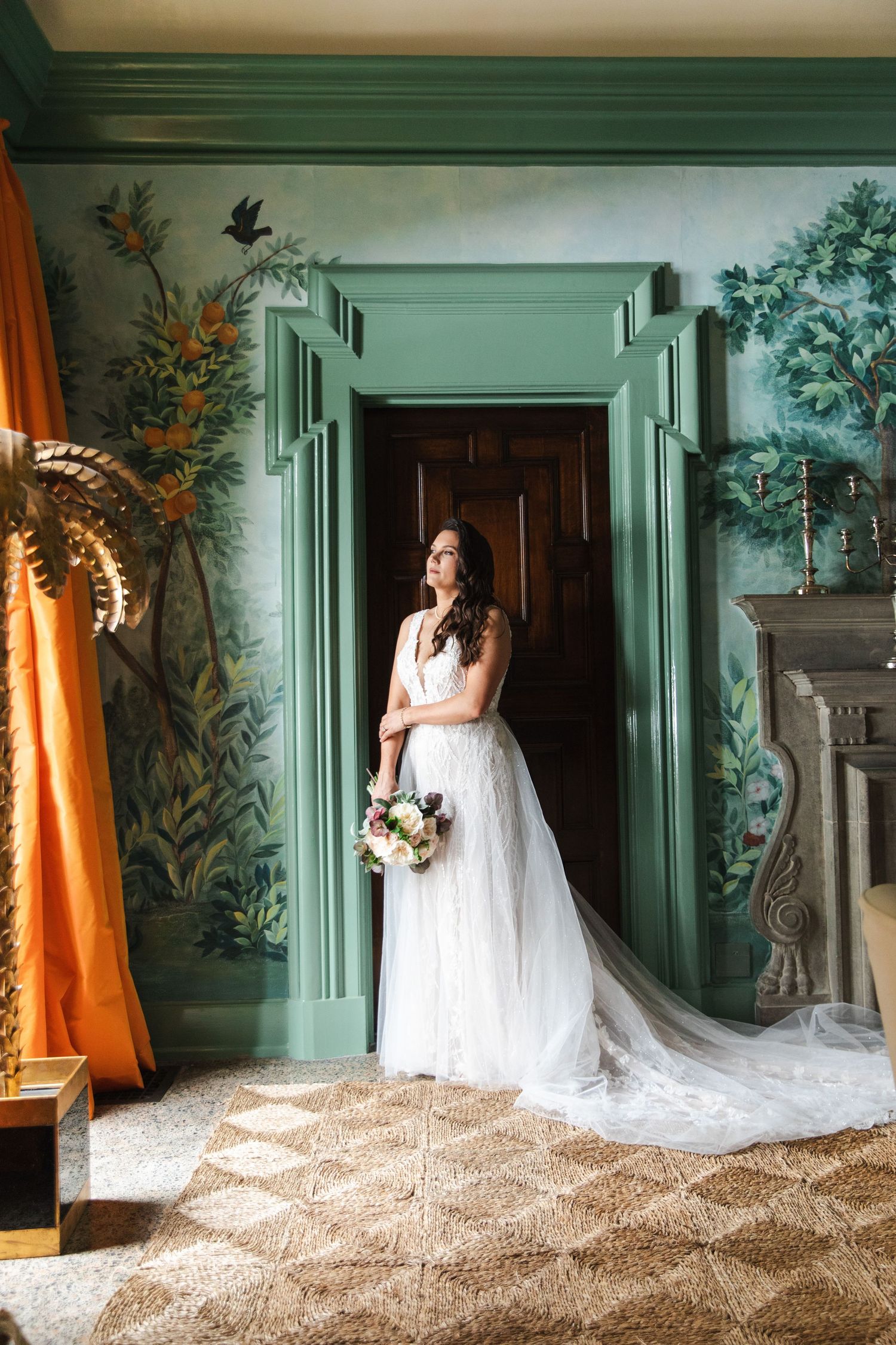 A stunning white wedding dress with a long train displayed in an elegant green-walled room with ornate decor.