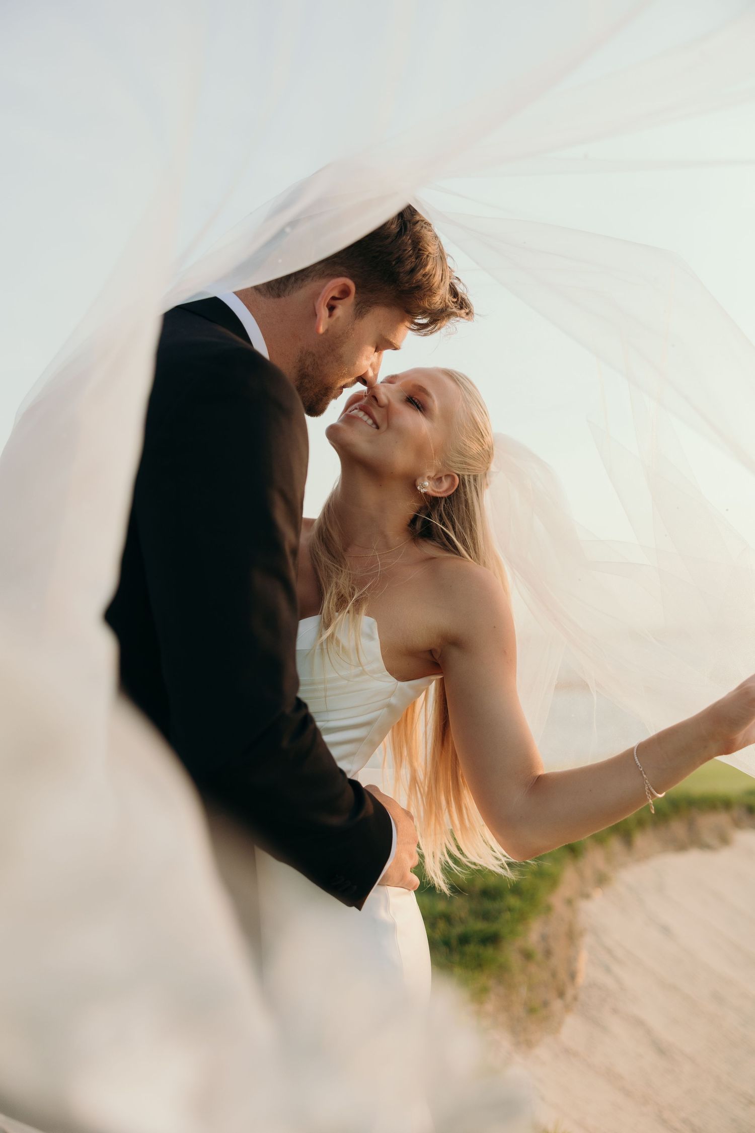 Romantic wedding photos under flowing white veil against soft natural lighting.