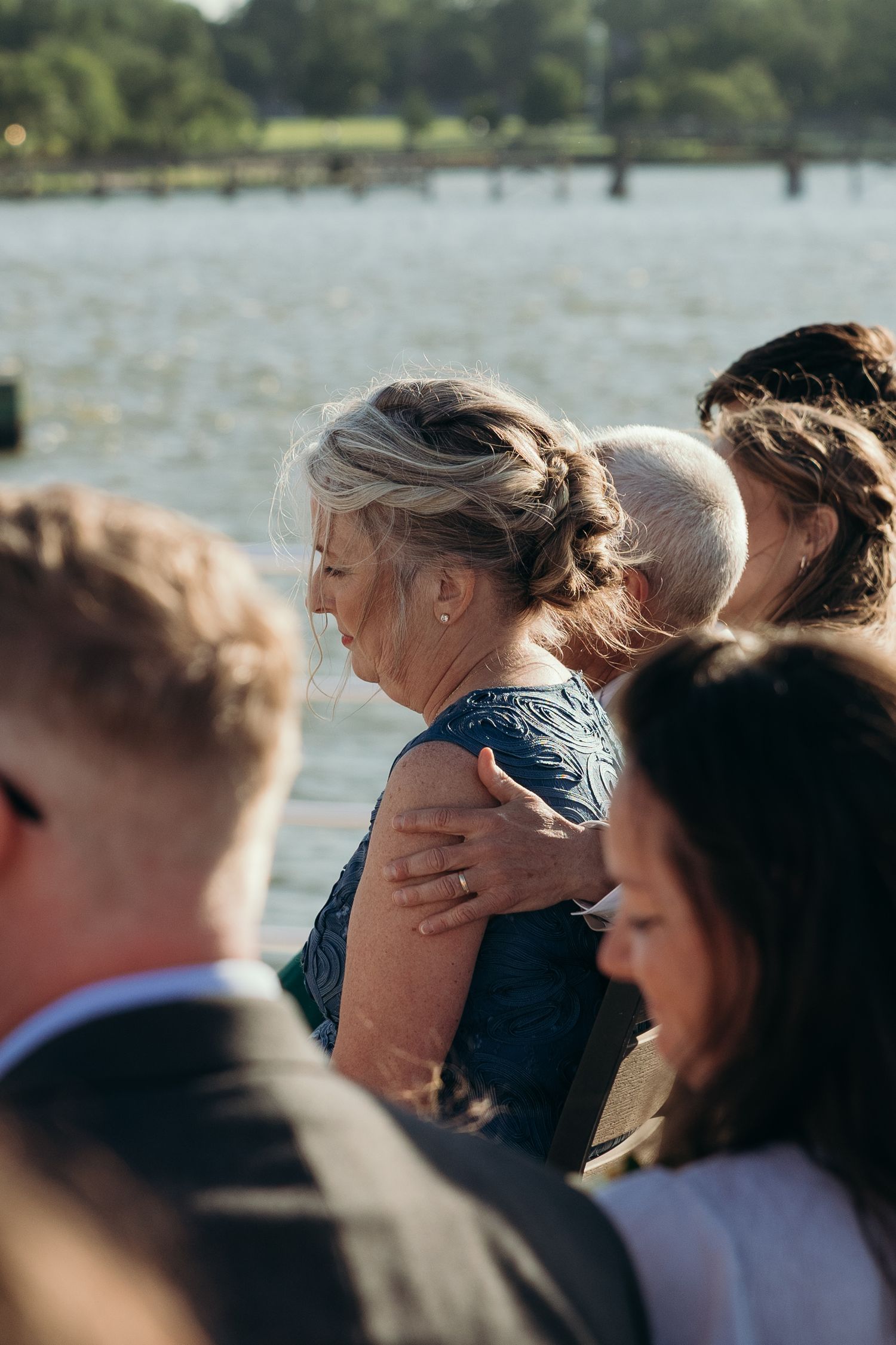 Wedding guests watch the ceremony against a waterfront backdrop.