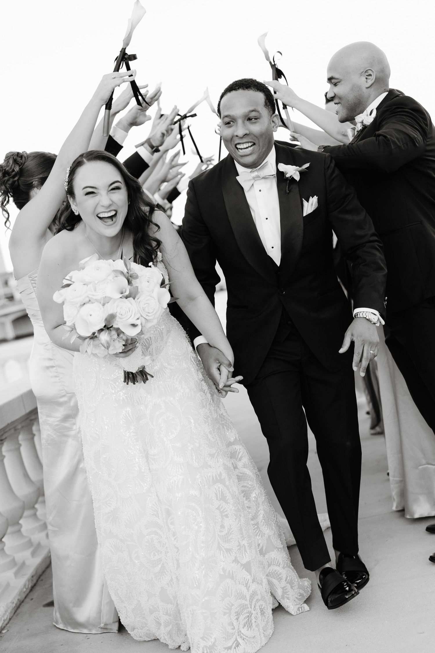 Wedding party celebrates joyfully in black and white on an outdoor terrace.