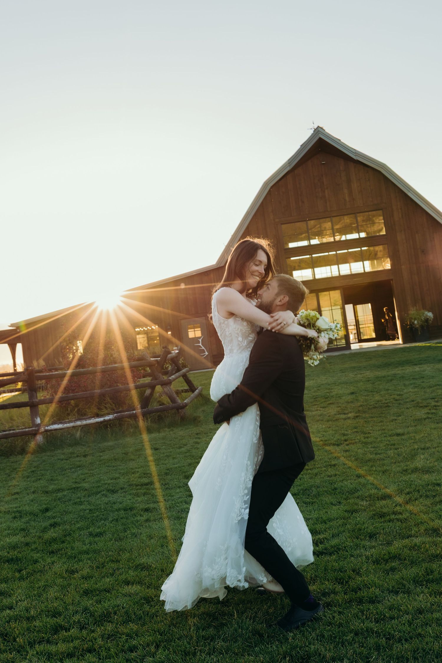 A couple dances and spins on a grassy hillside at sunset with a rustic barn in the background.