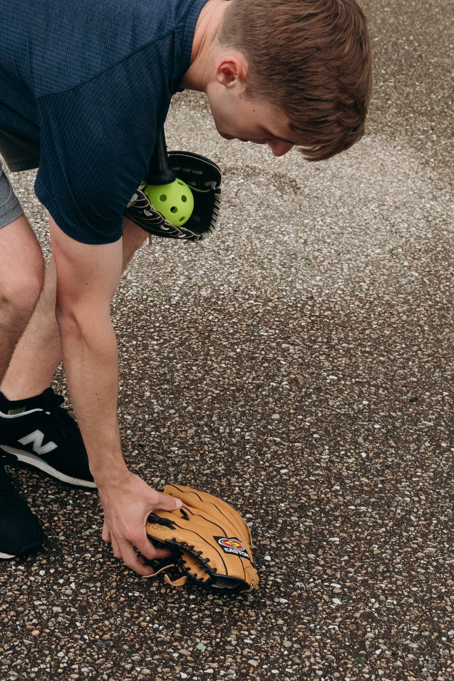 Person bending down to pick up a baseball with a leather glove.