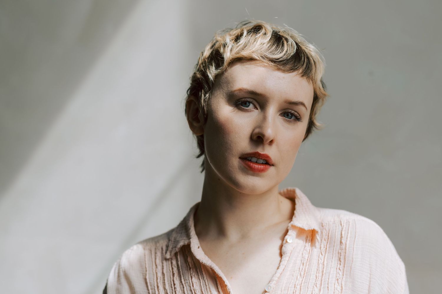 Portrait of a person with short blonde hair wearing a white blouse against a light background.