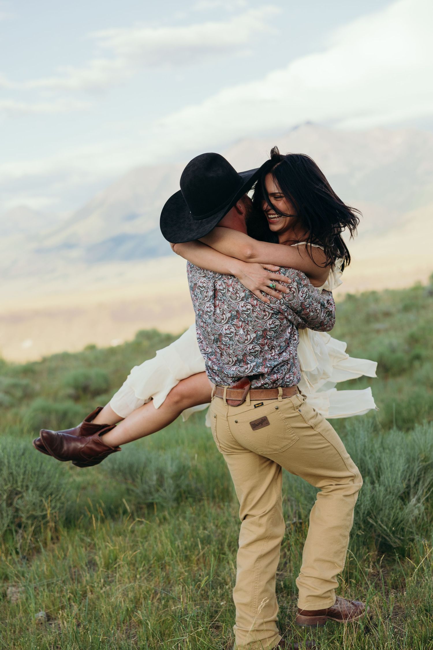A romantic dip pose between a couple in western attire on a scenic hillside.