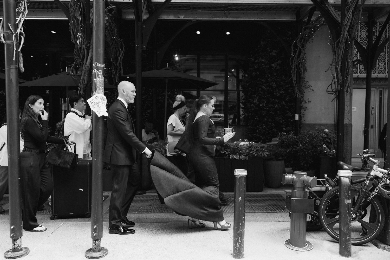 A vintage black and white photograph shows people outside a building entrance with a barber chair and motorcycle visible.