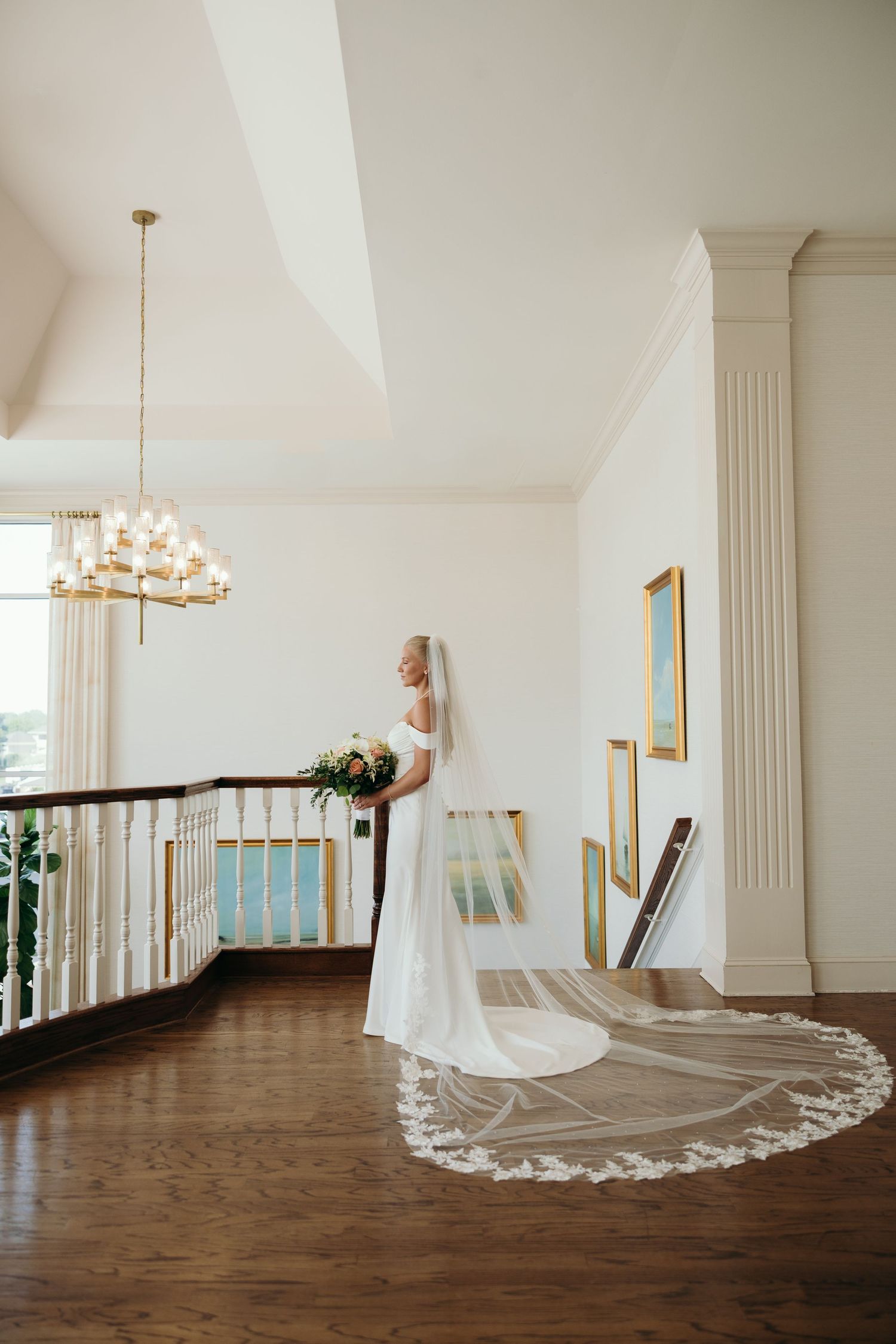 Wedding dress with long train displayed in an elegant white interior with hardwood floors.