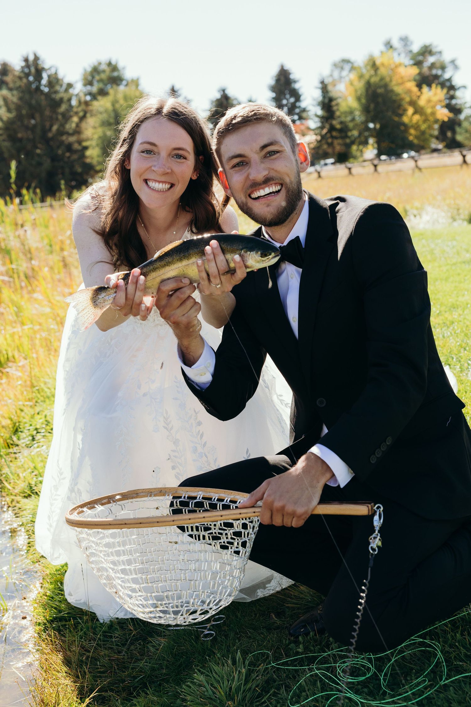 Couple shares joyful moments in a field with white lace dress and formal attire.