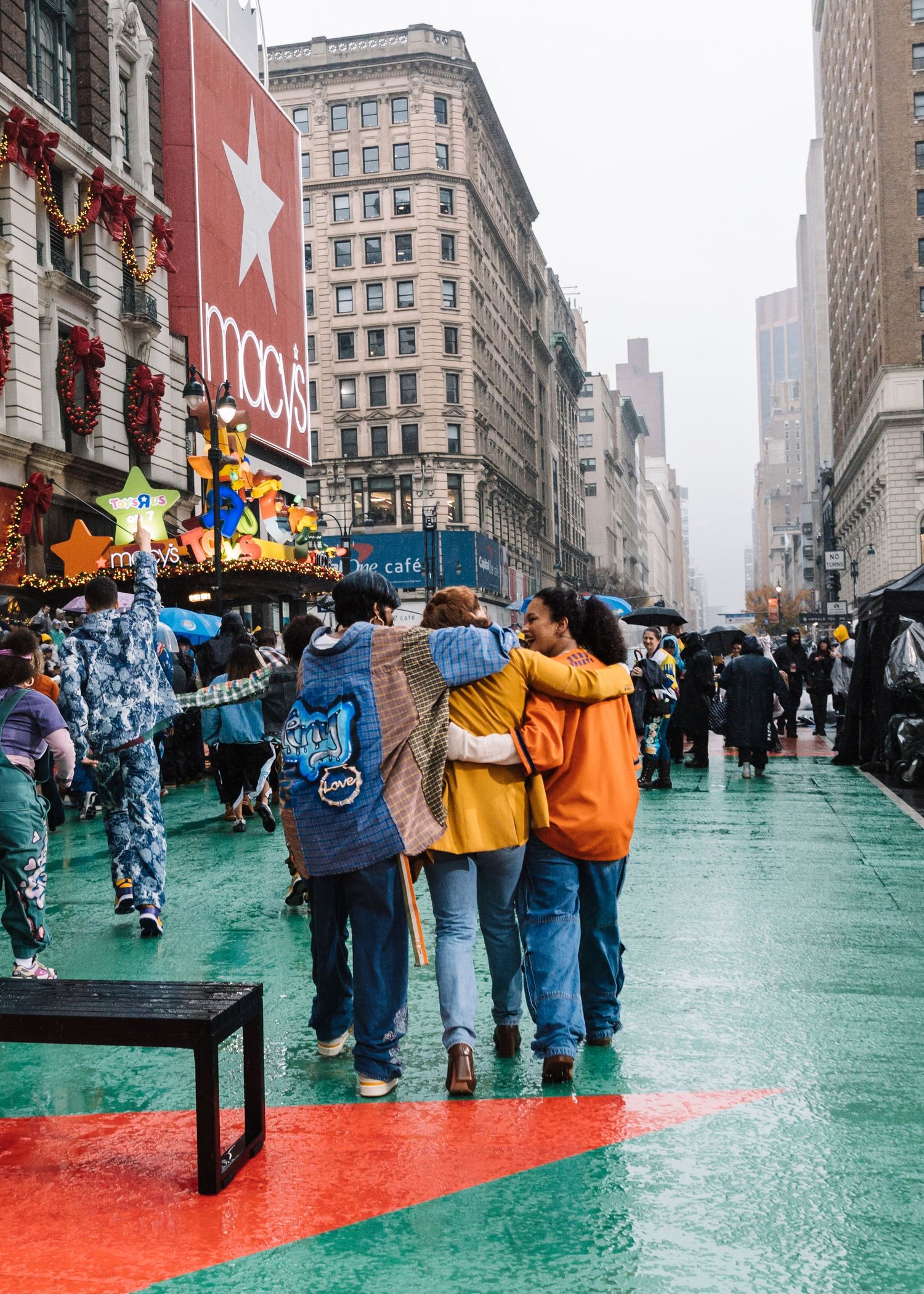 People walk together on a wet green street with classic New York architecture in the background.