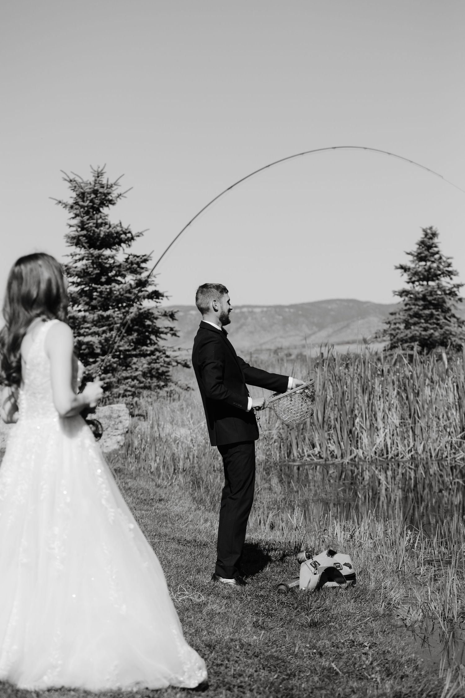 Black and white photo of couple in wedding attire playing with fishing rods in a field.
