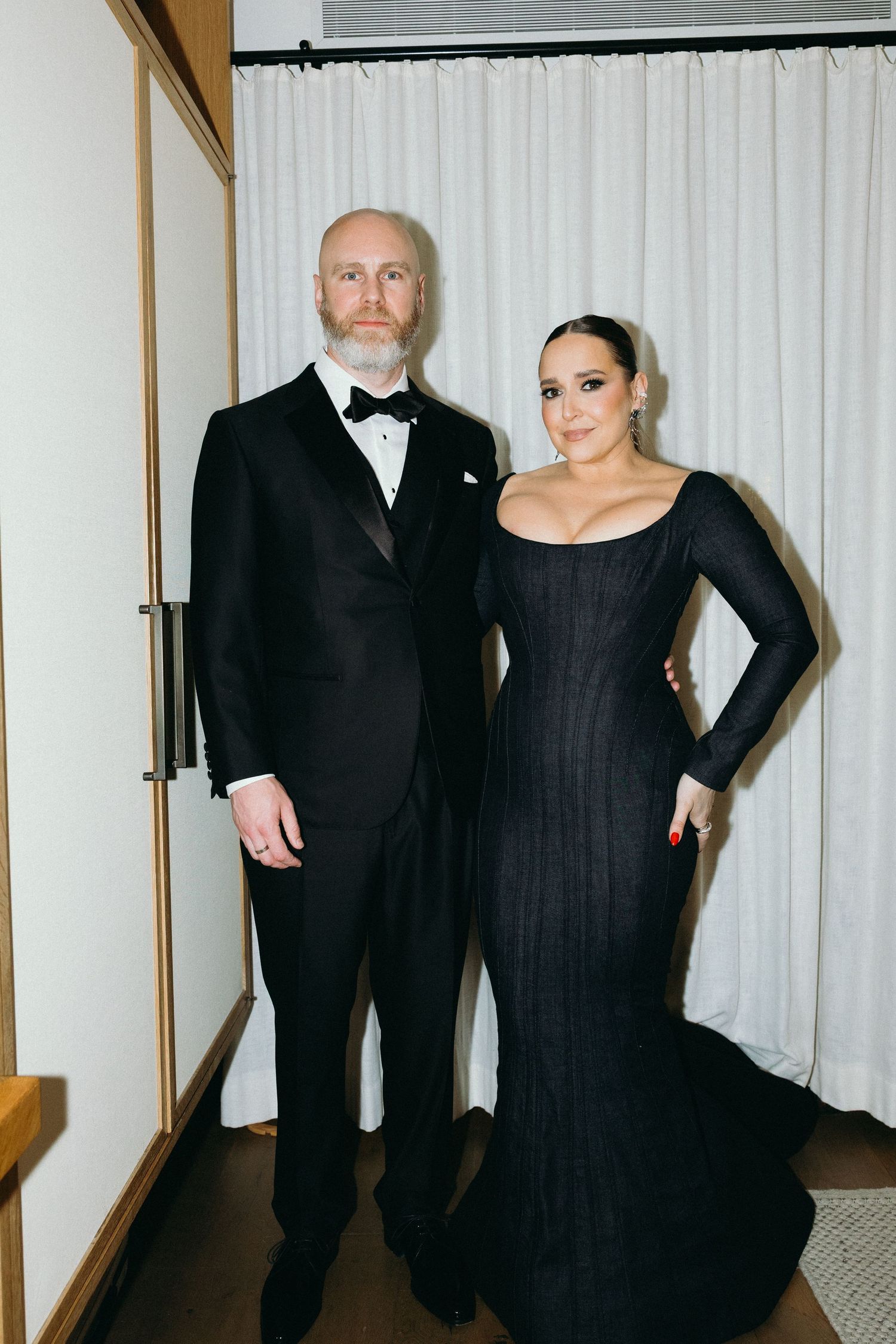 Jessica Vosk and Dave in formal black attire pose dramatically in front of a white curtain.