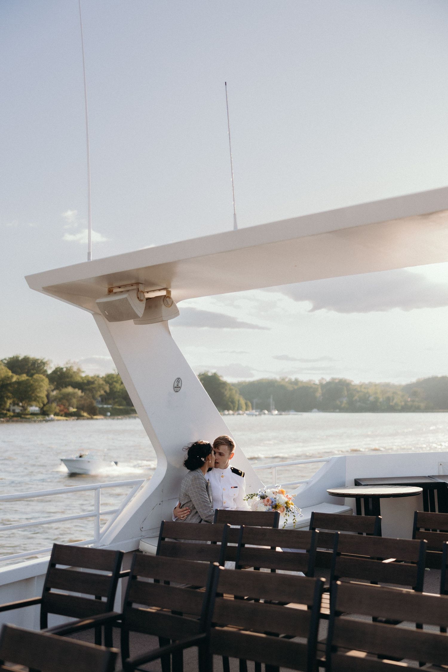 A romantic moment aboard a boat with water and shoreline visible in the background.