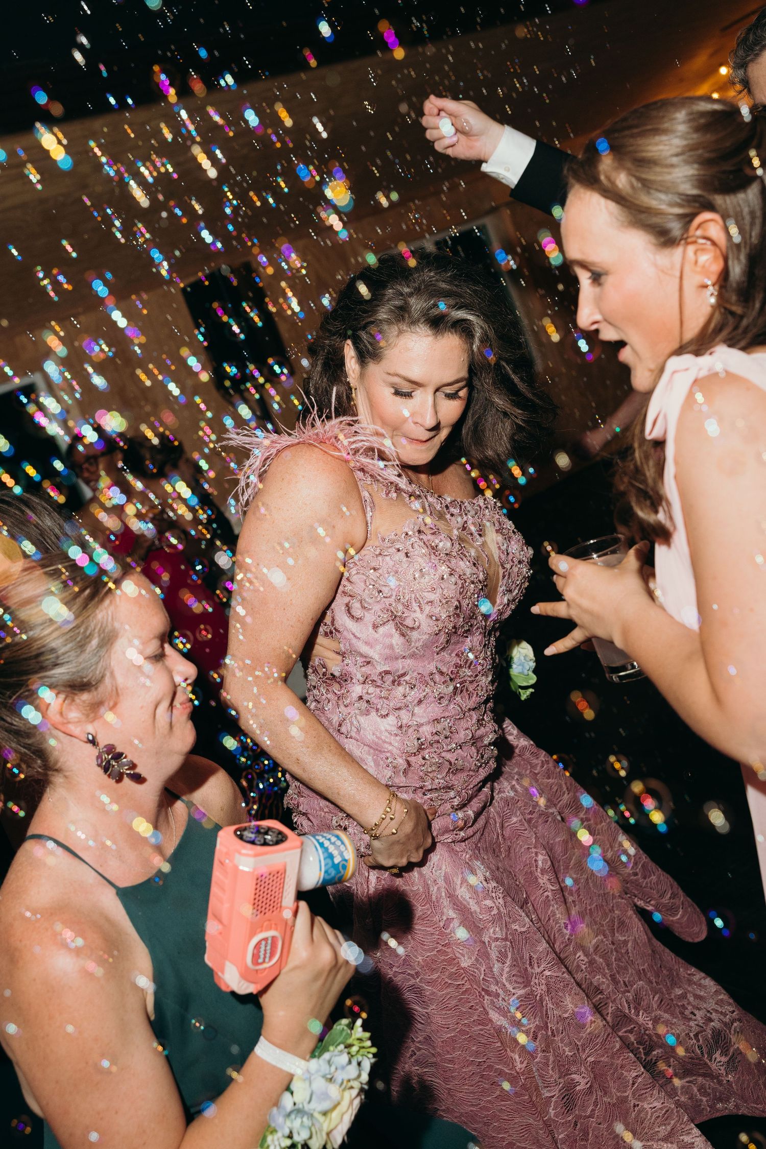 Women dancing joyfully at a wedding reception with confetti and bubbles filling the air around them.
