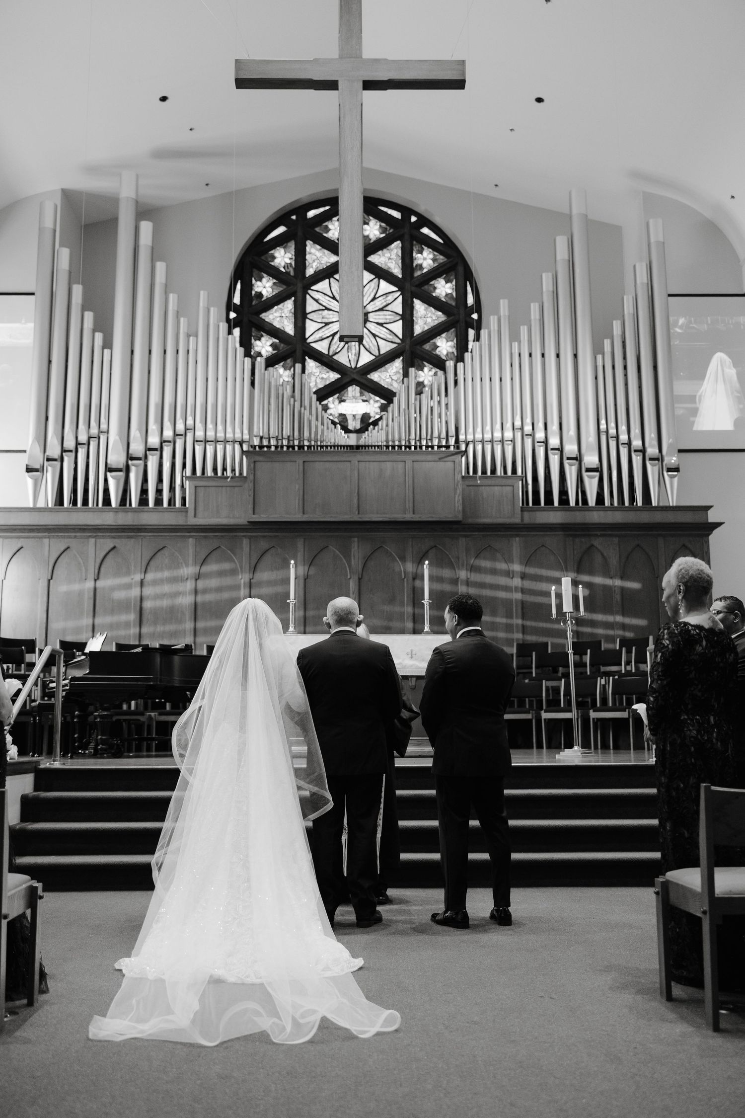 A wedding ceremony in a church sanctuary with white pews and large pipe organ in the background.