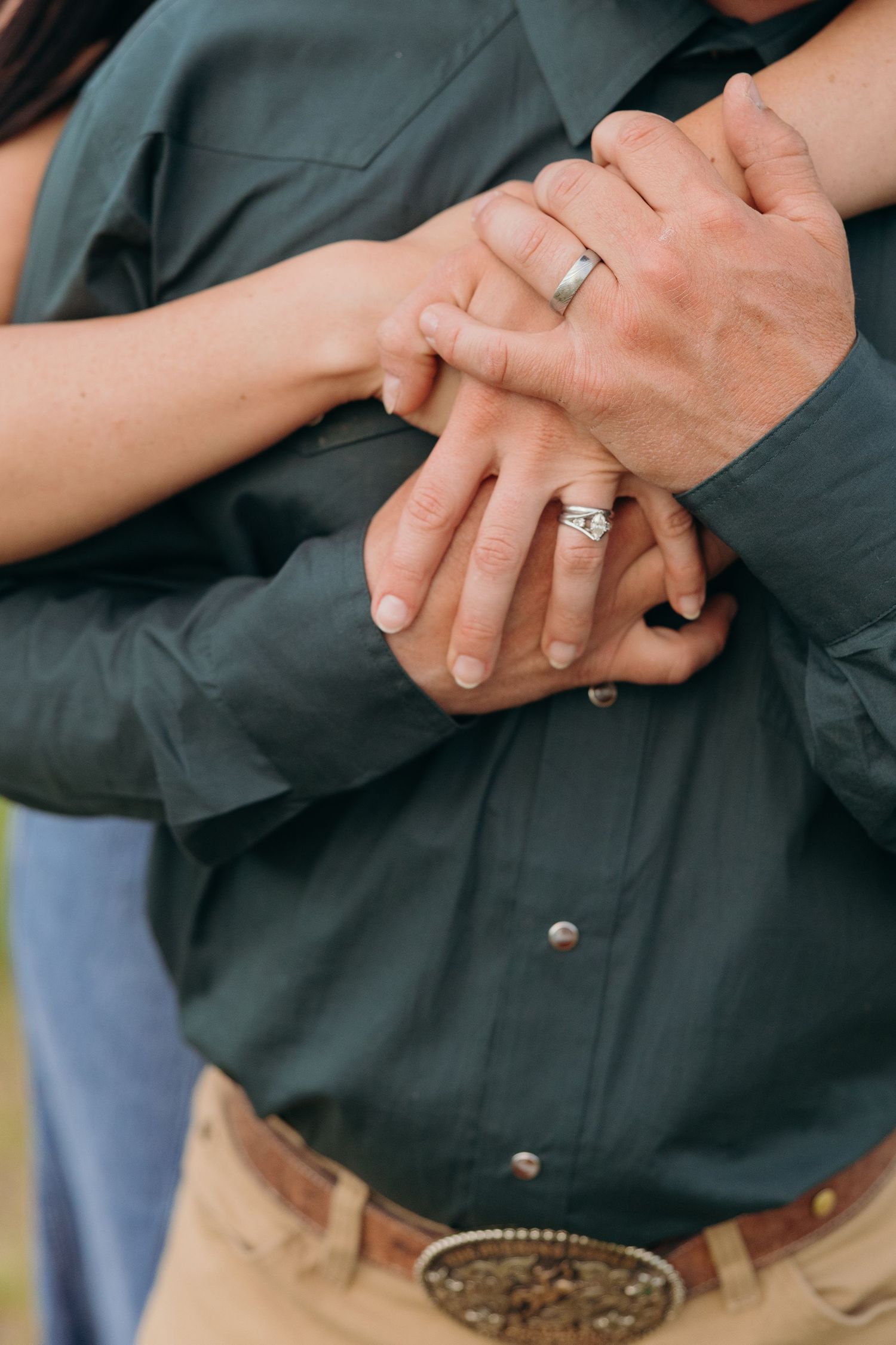 Close-up of intertwined hands showing engagement rings against casual clothing.