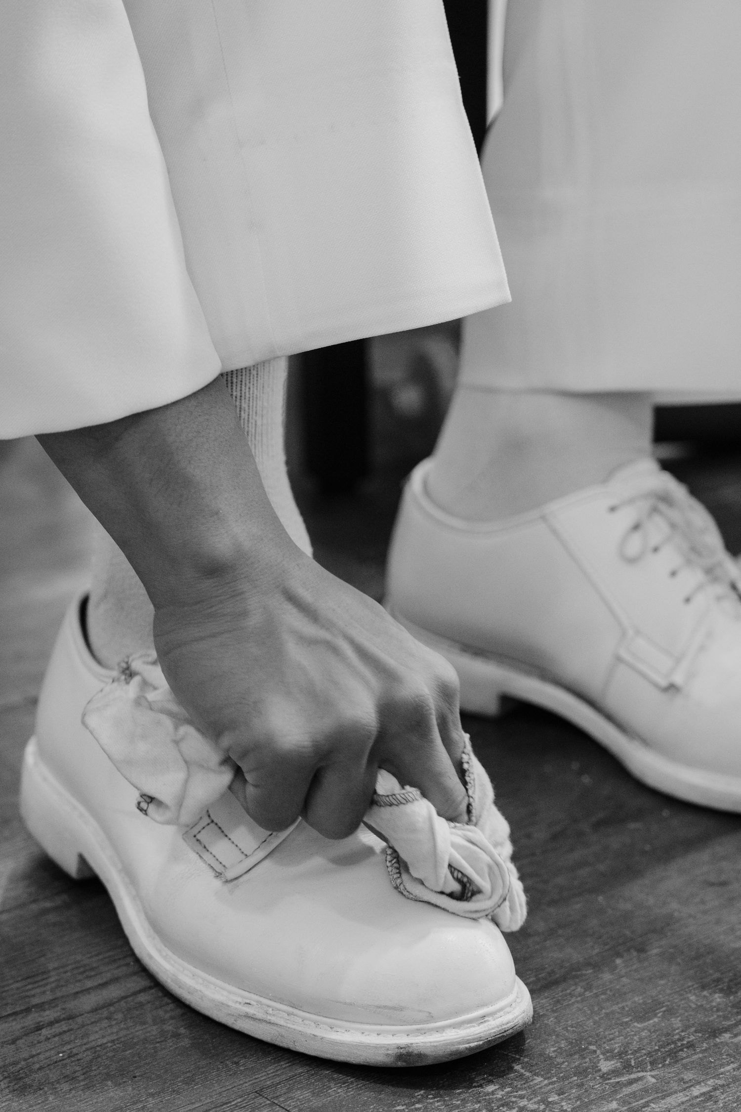 Close-up sequence showing someone polishing white dress shoes on a dark surface.