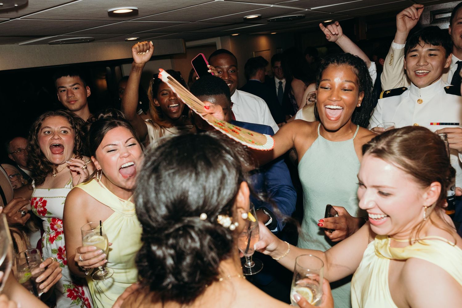 Energetic crowd dancing and celebrating with raised arms at a wedding reception.