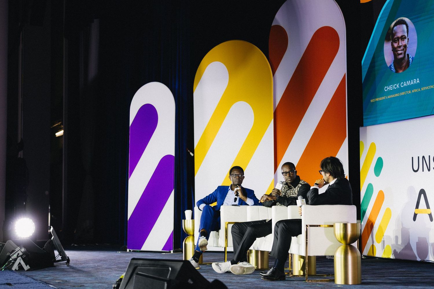 Conference stage setup with colorful diagonal striped backdrop panels and podium illuminated by spotlights.