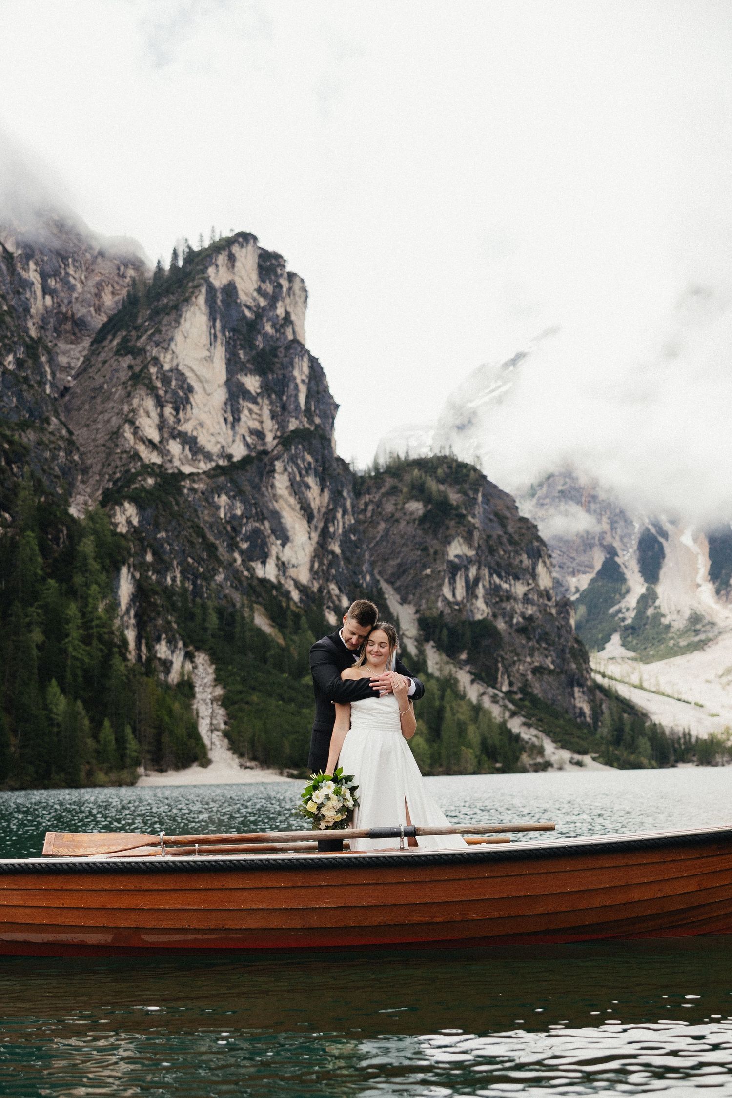 A romantic wedding moment captured on a wooden boat with majestic Dolomite mountains in the background.