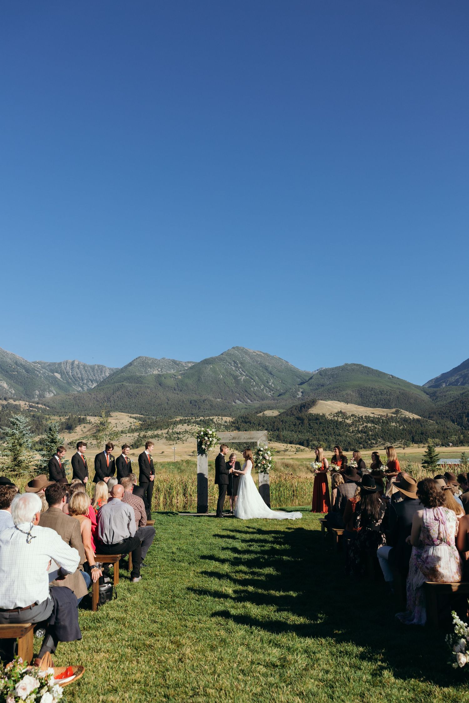 Panoramic view of outdoor wedding ceremony with mountain range and blue sky.