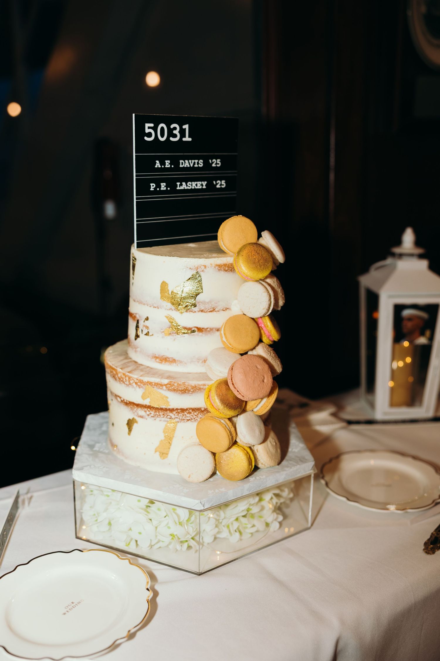 Elegant white wedding cake decorated with macarons and gold accents on display.